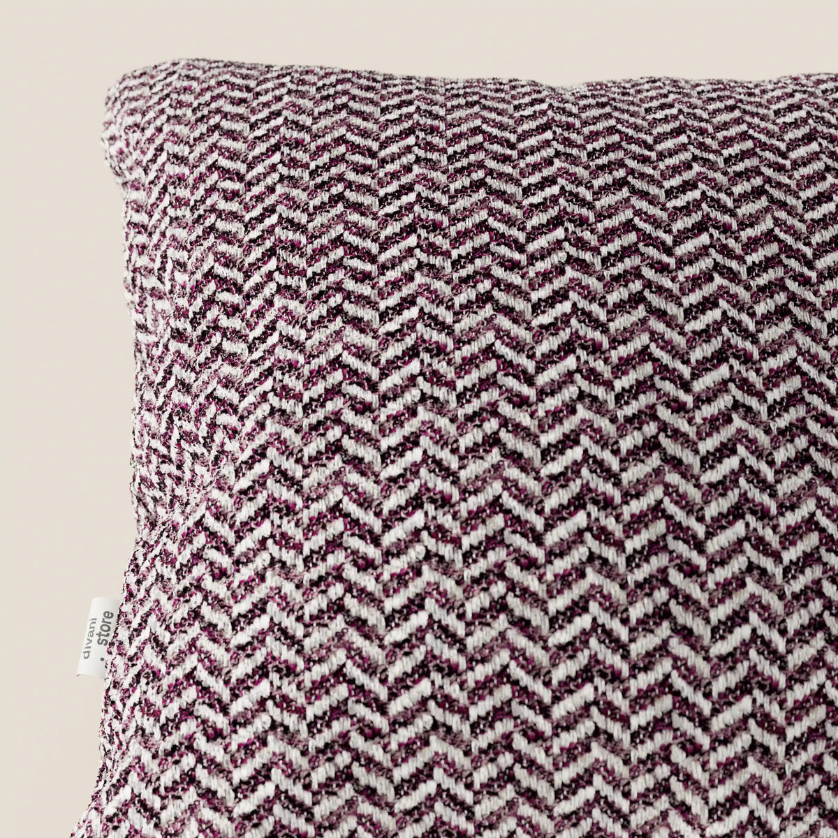 Un primo piano del cuscino Sorrento 45x45 in lino di divitt.sbs, caratterizzato da una trama a zigzag in rilievo nei toni del bordeaux e del bianco, lavabile in lavatrice. Una piccola etichetta bianca impreziosisce la cucitura sinistra, su uno sfondo beige neutro.
