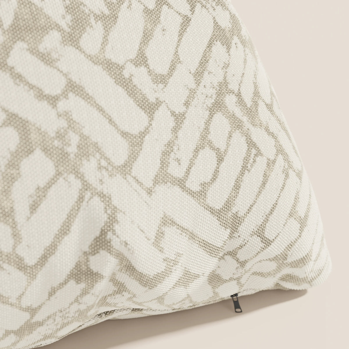 Primo piano del cuscino geometrico Brick di divitt.sbs, realizzato in tessuto idrorepellente beige con un motivo astratto bianco e grigio chiaro e una piccola etichetta nera sul bordo inferiore.