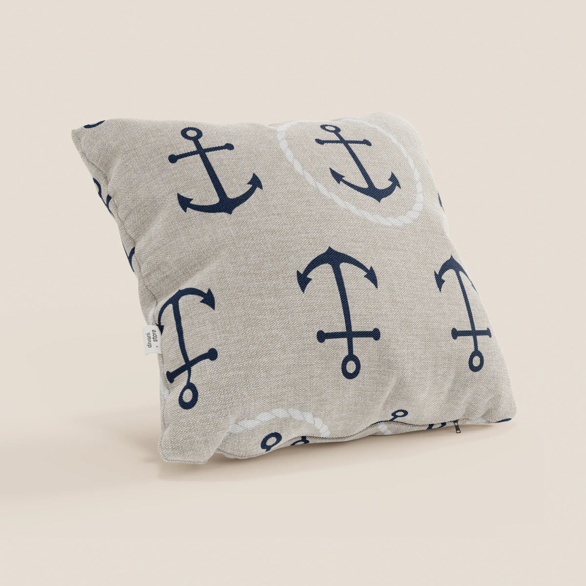 Il cuscino quadrato beige Nautilus di divitt.sbs, con motivi ancora blu navy e cerchi di corda bianchi, ha zip inferiore e piccola etichetta bianca. È lavabile in lavatrice, ideale per uno stile marino pratico ed elegante.