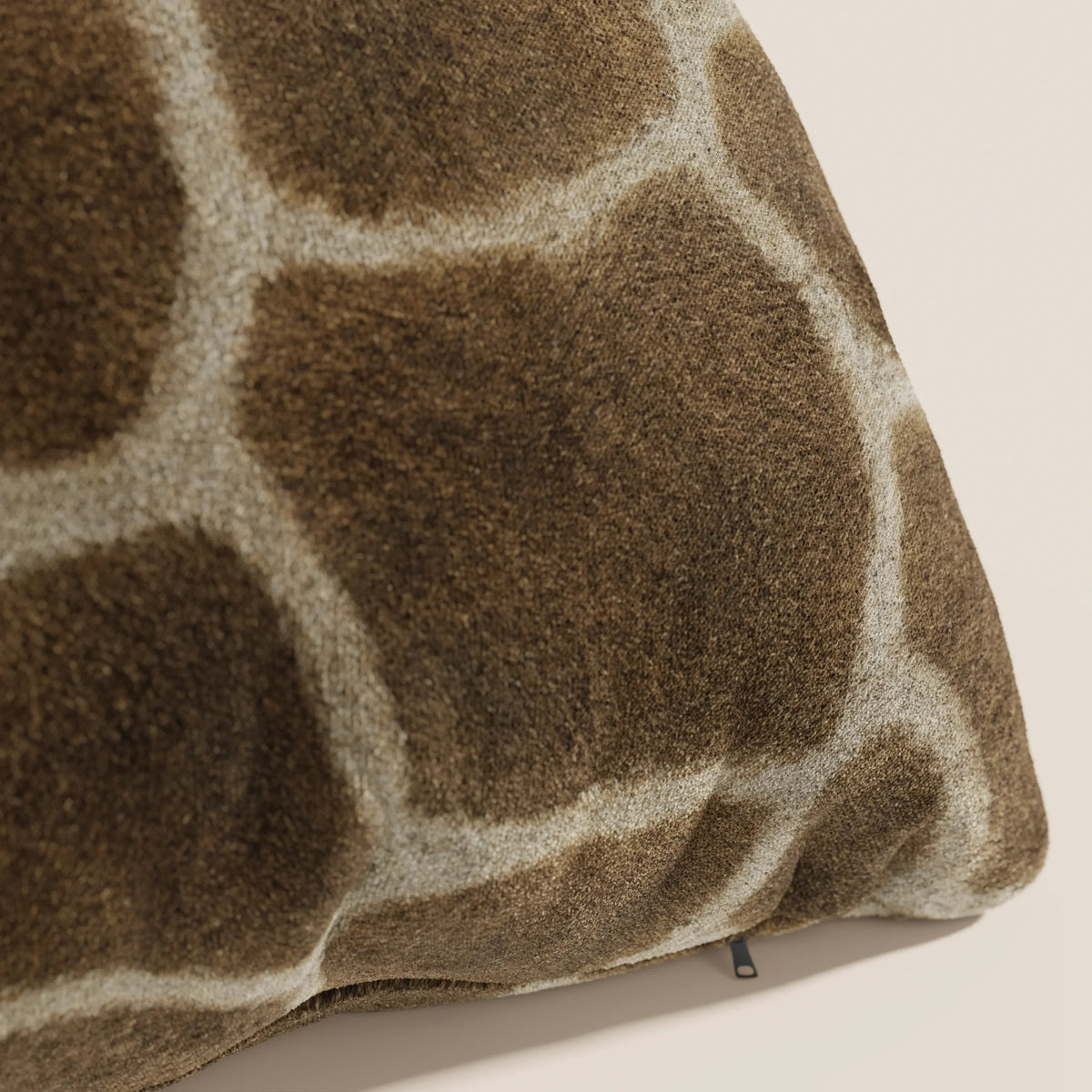 Un primo piano del cuscino Wild 45x45 della collezione Wild di divitt.sbs mostra la microfibra impermeabile a motivo di giraffa, di colore marrone con macchie chiare, dalla consistenza vellutata e con una raffinata targhetta nera lungo il bordo.