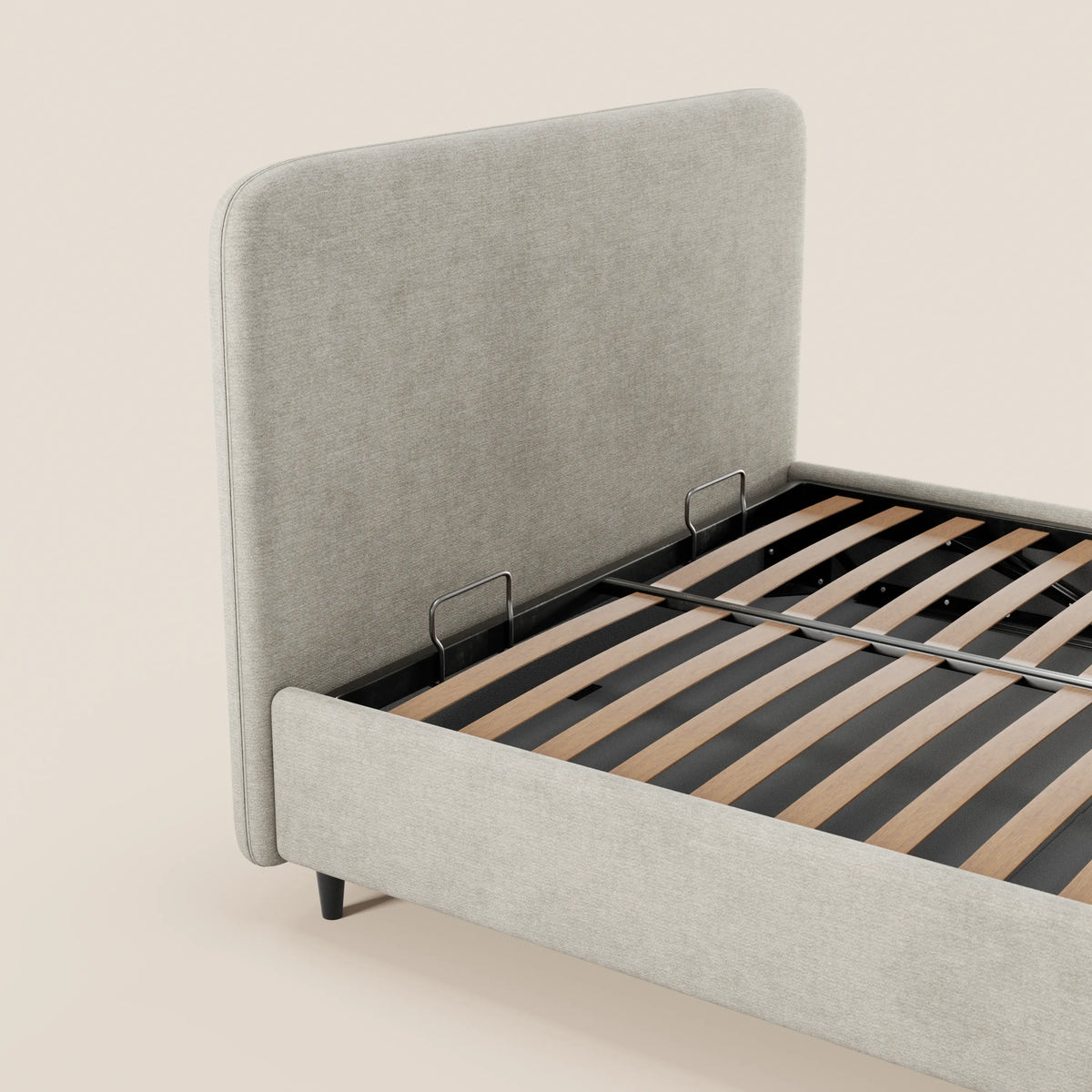 Il letto imbottito KAELOS minimal di Letti.store presenta una testiera arrotondata in ciniglia, gambe alte e un vano contenitore. Il rivestimento grigio chiaro e il design essenziale risaltano sullo sfondo beige, con doghe in legno scuro e due supporti in metallo.