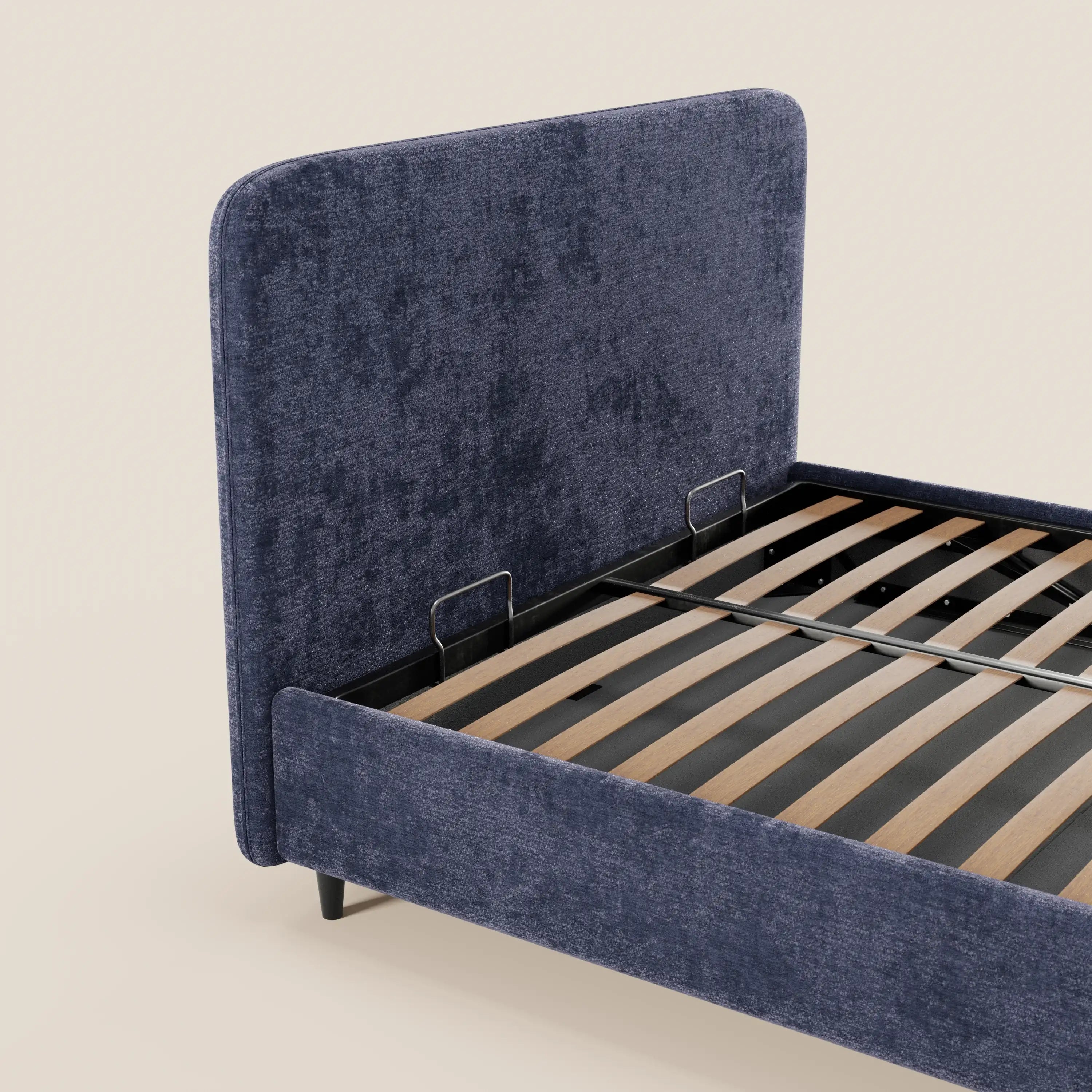Il letto imbottito KAELOS minimal di Letti.store presenta una testiera arrotondata in tessuto chenille, piedini alti, un vano contenitore e una base a doghe in legno con travi di sostegno nere, il tutto su uno sfondo beige chiaro.