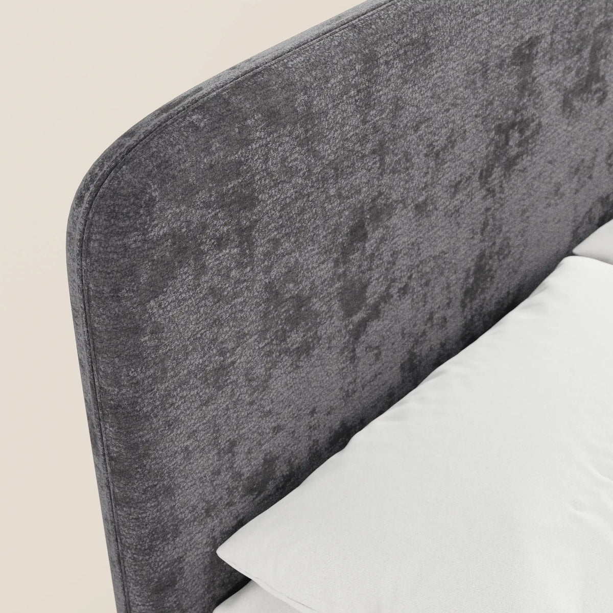 Primo piano del letto imbottito KAELOS Letto Minimal di Letti.store: testiera arrotondata rivestita in ciniglia grigia, gambe alte, vano contenitore, raffigurato accanto a un cuscino bianco e a un materasso su uno sfondo beige — ideale per una camera da letto moderna.