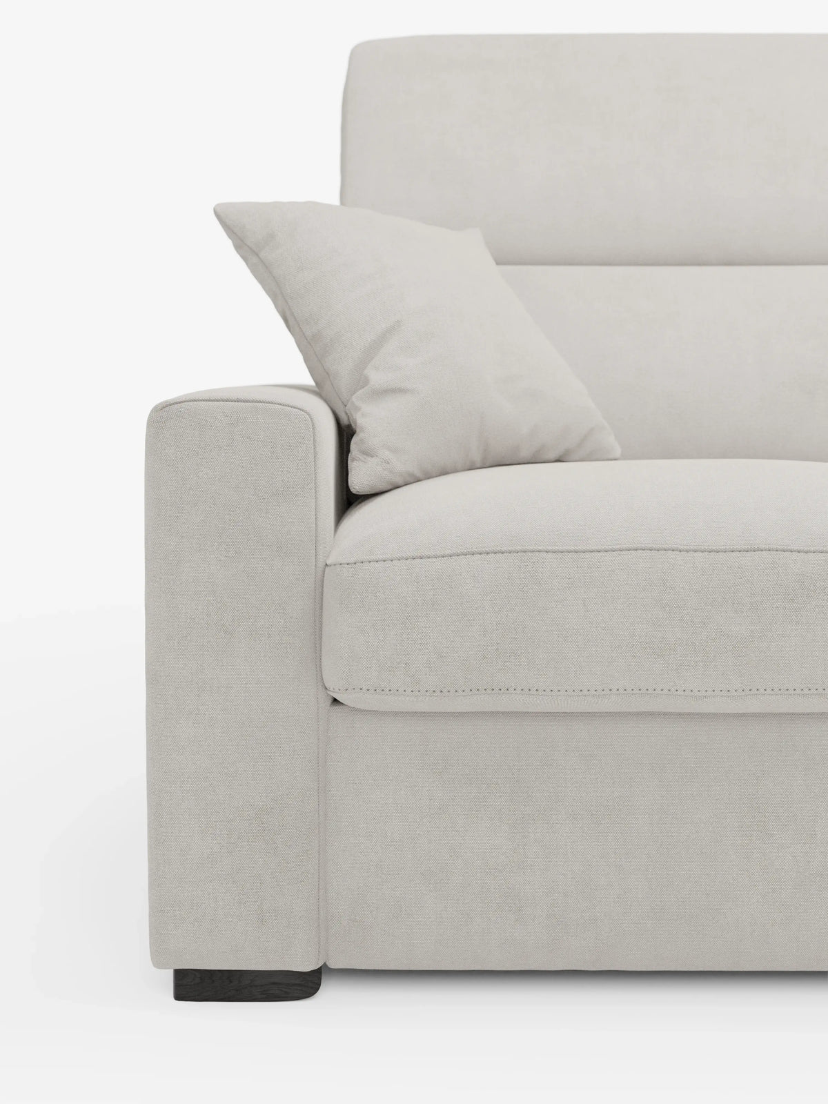 Primo piano del divano letto Maximus a 3 posti con materasso ALTO da 20 cm di divitt.sbs in una tonalità beige chiaro, che mette in risalto il bracciolo sinistro, il cuscino di seduta e lo schienale. Un cuscino decorativo abbinato è appoggiato allo schienale e al bracciolo. Il rivestimento è realizzato in un morbido tessuto simile alla pelle scamosciata, certificato Oeko-Tex e resistente alle macchie, con cuciture a vista e piedini in legno. I poggiatesta reclinabili aggiungono ulteriore comfort e