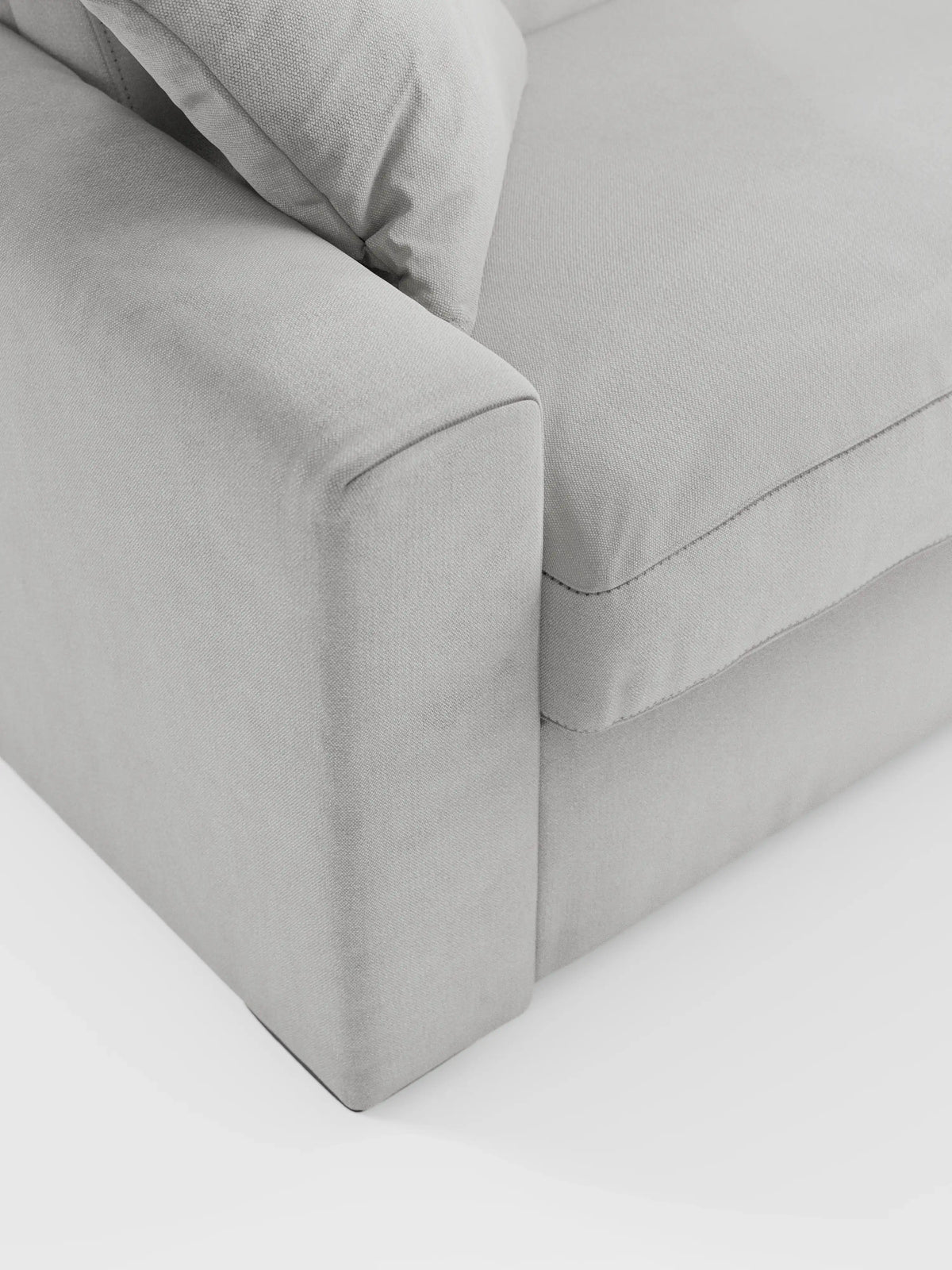 Primo piano dell'angolo del divano letto a 3 posti Maximus con materasso ALTO da 20 cm di divitt.sbs, con bracciolo, cuscino di seduta e cuscino dello schienale realizzati in un moderno tessuto grigio chiaro Oeko-Tex antimacchia, caratterizzato da linee morbide e pulite e da cuciture minimaliste — raffigurato su sfondo bianco.