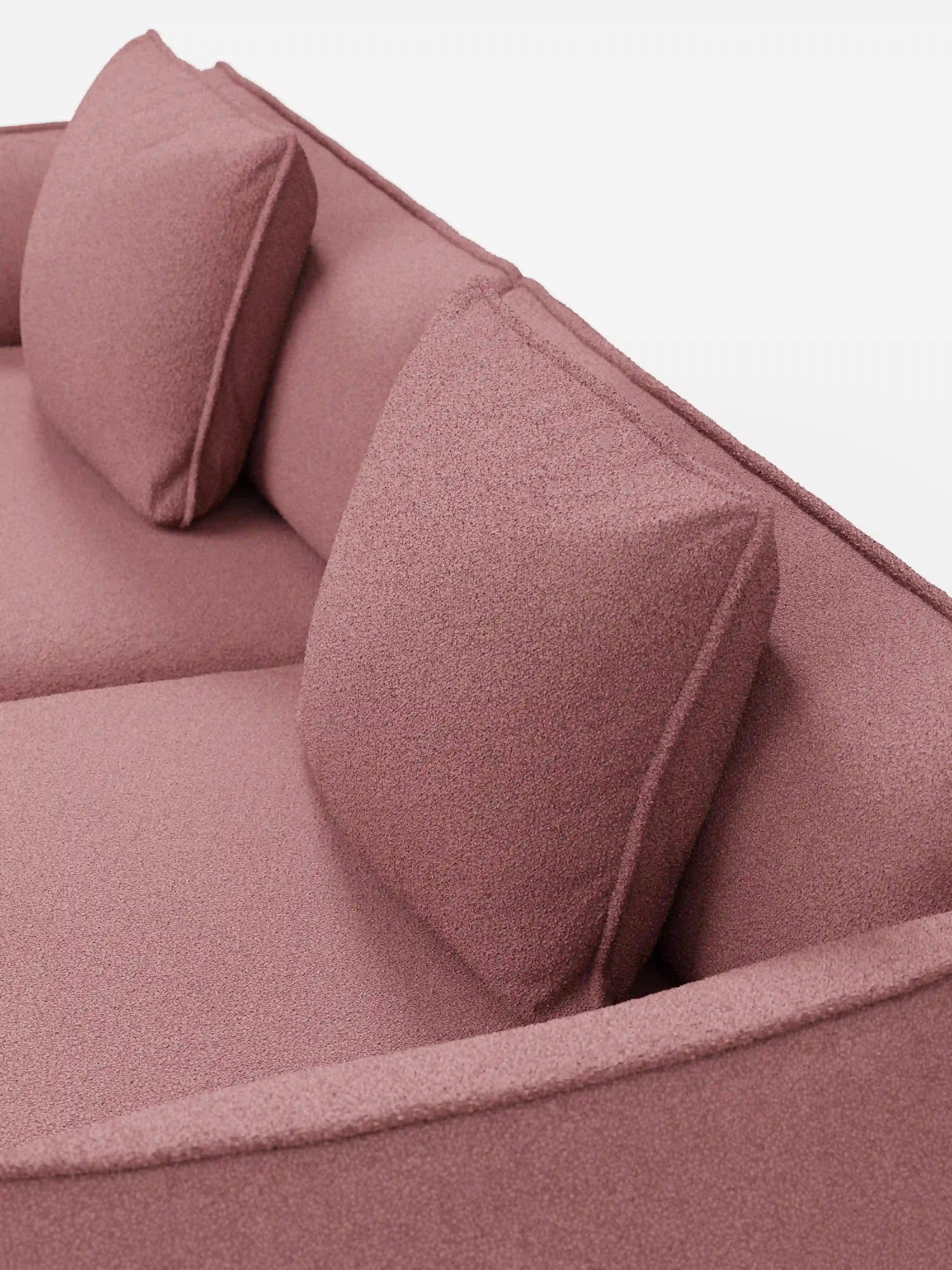 Un primo piano del divano Nimbus a 3 posti, modulare e componibile da 250 cm di divitt.sbs, presenta un rivestimento in tessuto T33 antimacchia color rosa polveroso con effetto cotone. Due cuscini quadrati coordinati per lo schienale e una seduta imbottita accentuano il design moderno, con il tessuto testurizzato che risalta su uno sfondo bianco luminoso.