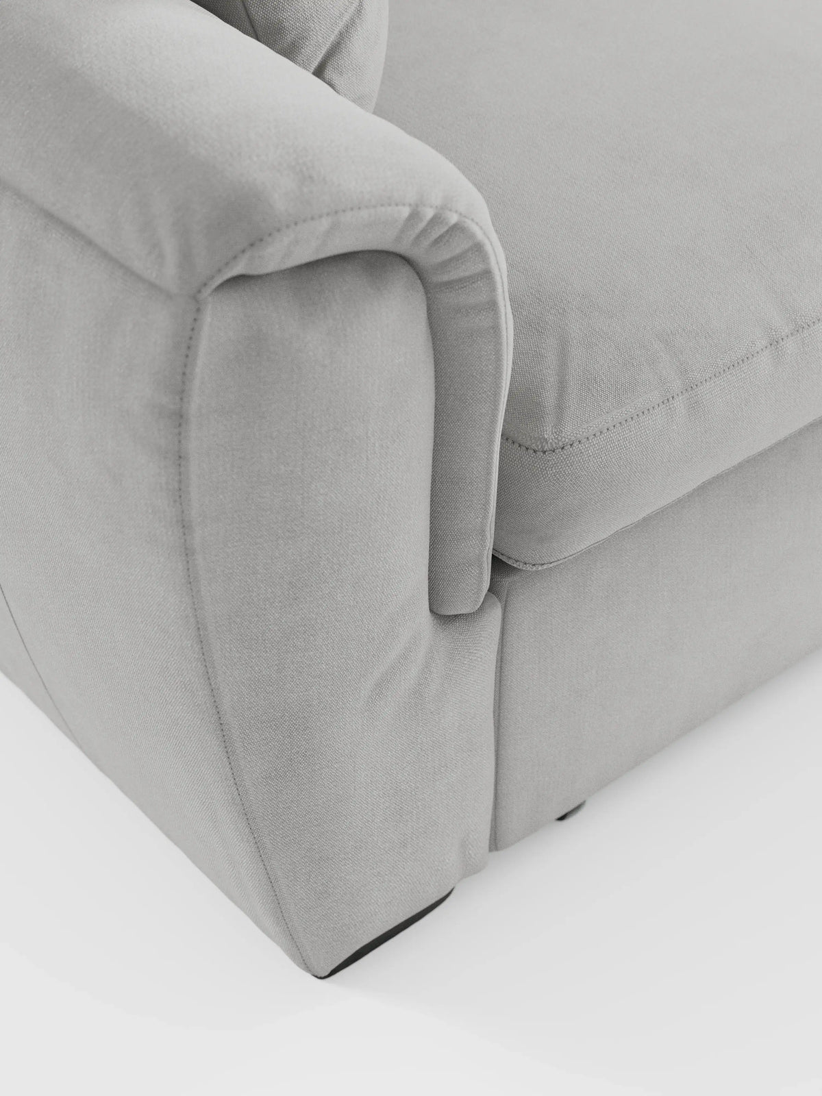 Primo piano del divano angolare reversibile con contenitore estraibile e pouf Titano, di colore grigio chiaro, di divitt.sbs, con i cuscini dei braccioli e della seduta. Il tessuto Oeko-Tex®, liscio e facile da pulire, presenta sottili dettagli di cucitura e una trama raffinata su uno sfondo bianco a tinta unita. Questa immagine mette in risalto il design morbido e arrotondato e i contorni delicati di questo divano versatile dotato di poggiatesta regolabili.