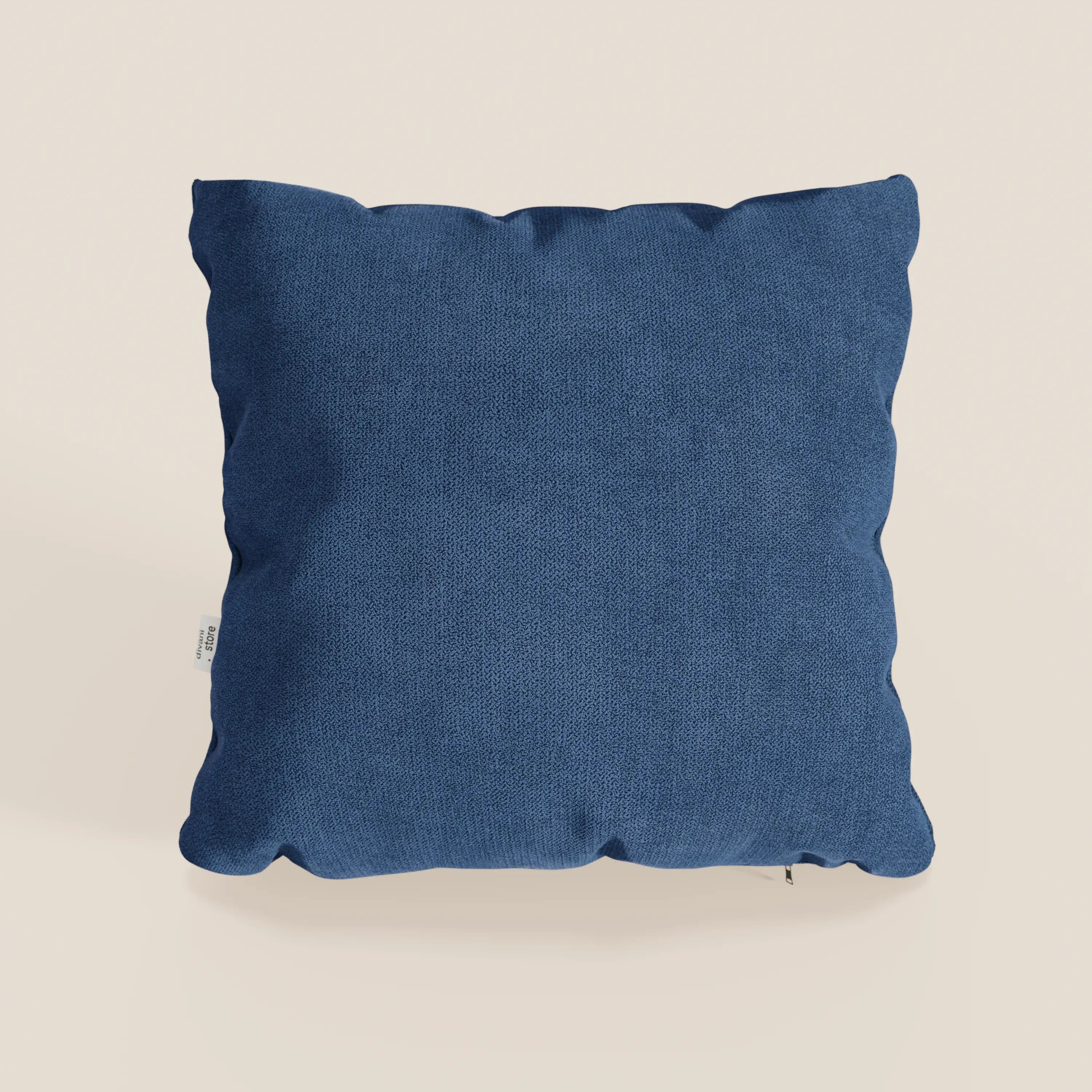 Il cuscino Destiny di divitt.sbs, 45x45 cm in morbido tessuto impermeabile blu T02, ha una forma quadrata, una superficie strutturata e una targhetta bianca sul bordo sinistro. Su uno sfondo neutro con ombre che ne evidenziano la morbidezza.