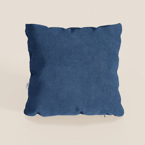 Il cuscino Destiny di divitt.sbs, 45x45 cm in morbido tessuto impermeabile blu T02, ha una forma quadrata, una superficie strutturata e una targhetta bianca sul bordo sinistro. Su uno sfondo neutro con ombre che ne evidenziano la morbidezza.