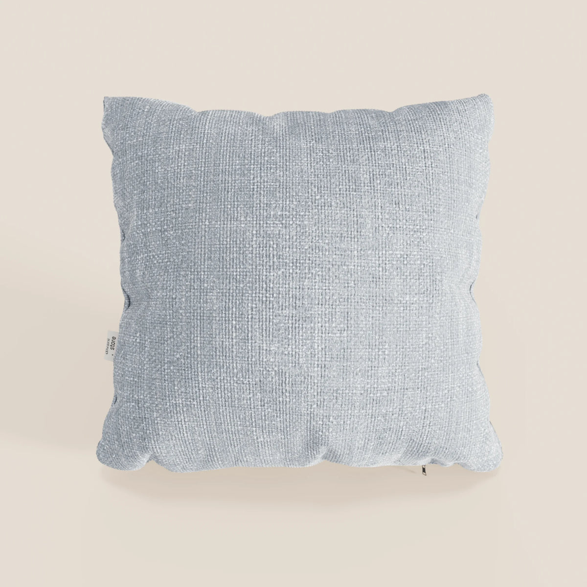 Il cuscino Lyon di divitt.sbs, 45x45 cm in T06 ghiaccio azzurro, è caratterizzato da un tessuto morbido intrecciato impermeabile e da una piccola targhetta bianca sul bordo sinistro, su un semplice sfondo bianco sporco.