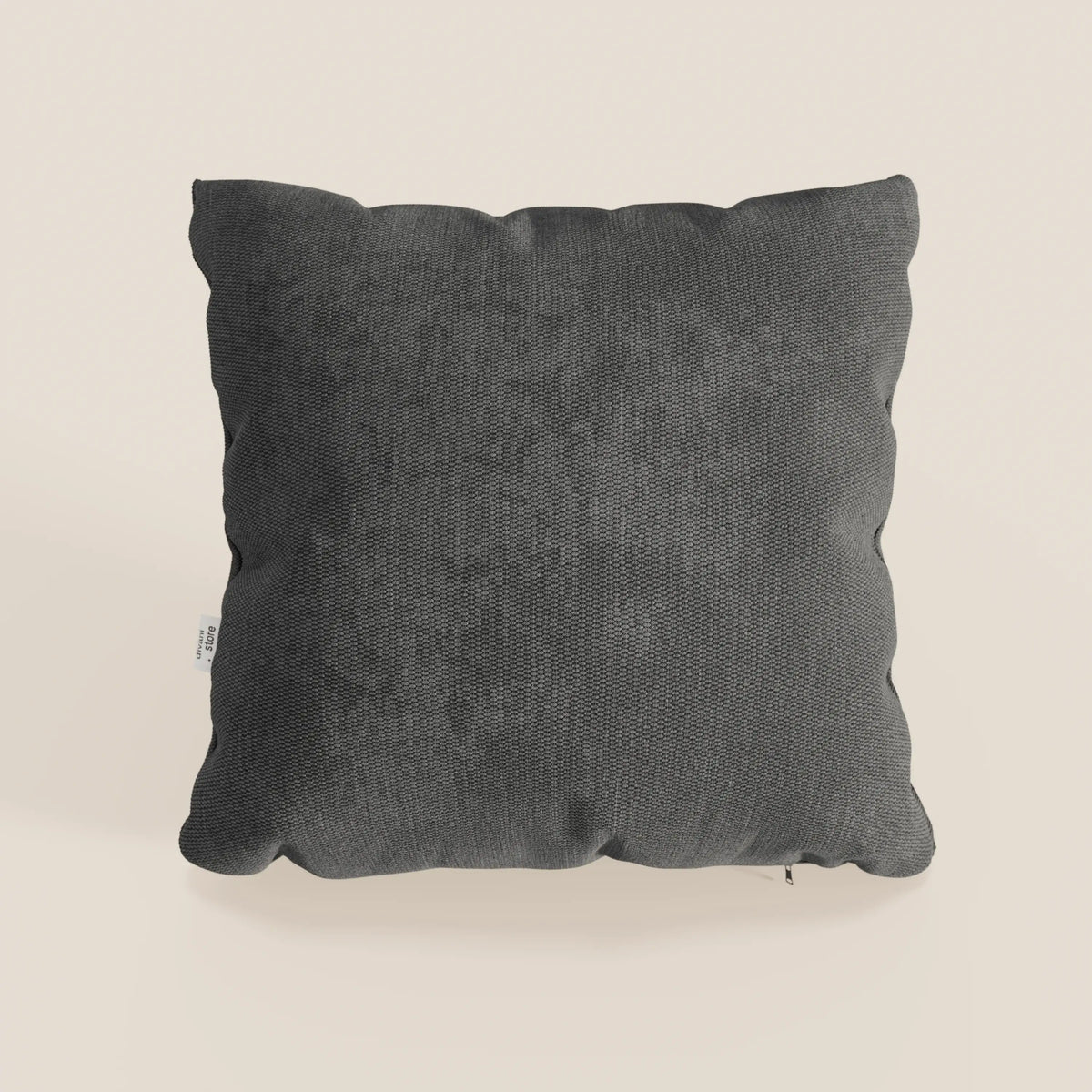 Il cuscino Miami di divitt.sbs, presentato nel colore antracite T14 morbido tessuto impermeabile, è un cuscino decorativo quadrato di colore grigio scuro con una finitura morbida e strutturata e sottili pieghe, caratterizzato da una piccola etichetta bianca sul lato sinistro.
