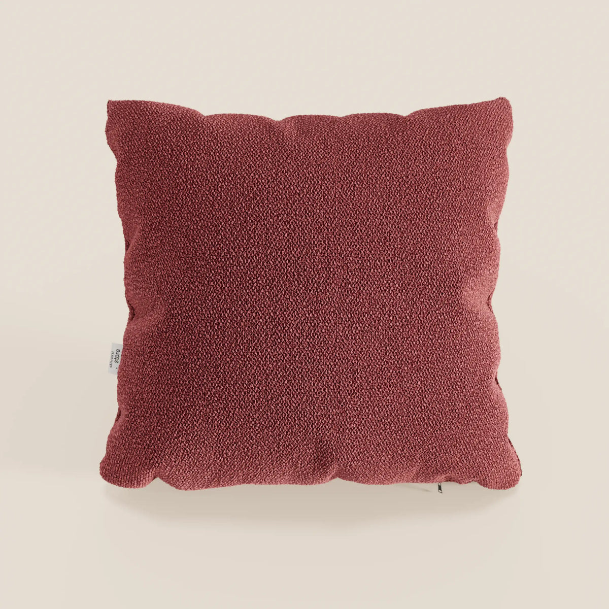 Il cuscino quadrato Lambada di divitt.sbs, di colore rosso intenso e realizzato in fresco tessuto simil-cotone impermeabile e antimacchia (T33), è posto al centro di un semplice sfondo beige. Ha un aspetto felpato, con angoli arrotondati e una piccola etichetta sulla sinistra.