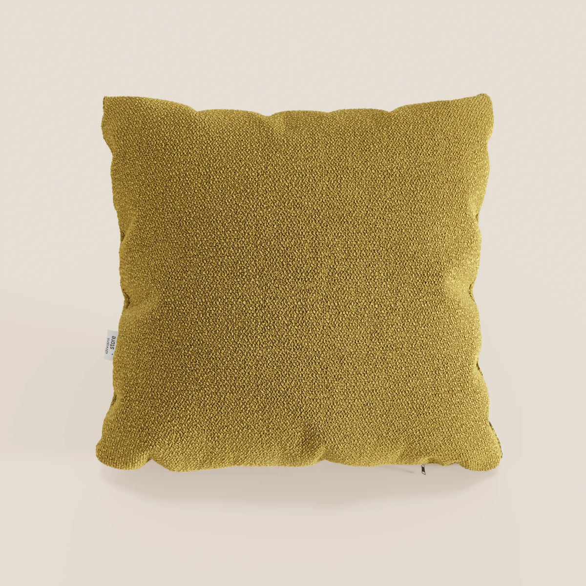 Un cuscino Lambada quadrato giallo senape di divitt.sbs si trova al centro di uno sfondo beige chiaro. Realizzato in fresco tessuto simil-cotone T33, antimacchia e impermeabile, presenta una consistenza morbida e un'etichetta in tessuto sul bordo sinistro.
