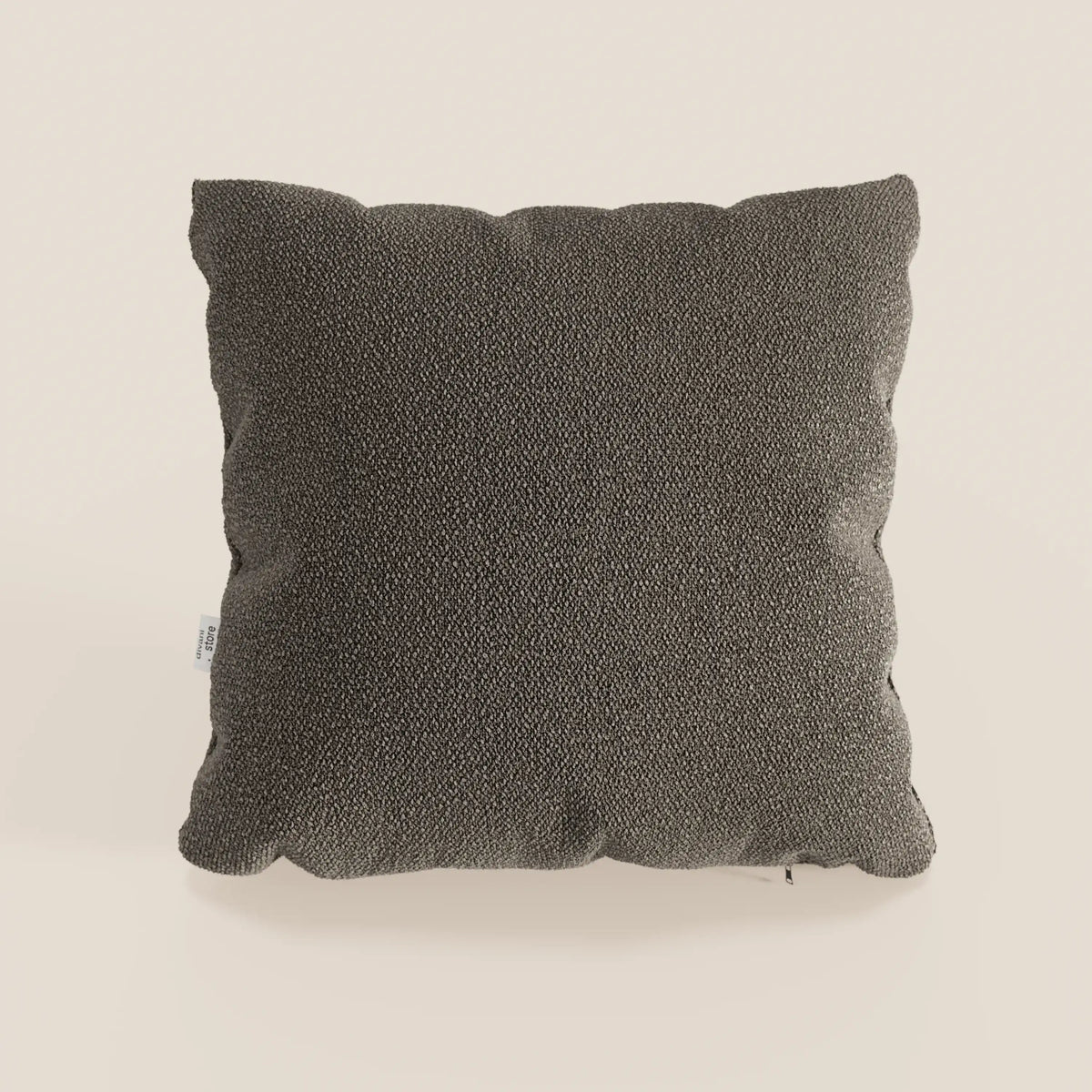 Un cuscino singolo Lambada grigio scuro di divitt.sbs, realizzato in tessuto fresco, antimacchia e impermeabile tipo cotone T33, è presentato con bordi felpati e un'etichetta laterale bianca su uno sfondo beige chiaro. Il design è semplice e moderno.