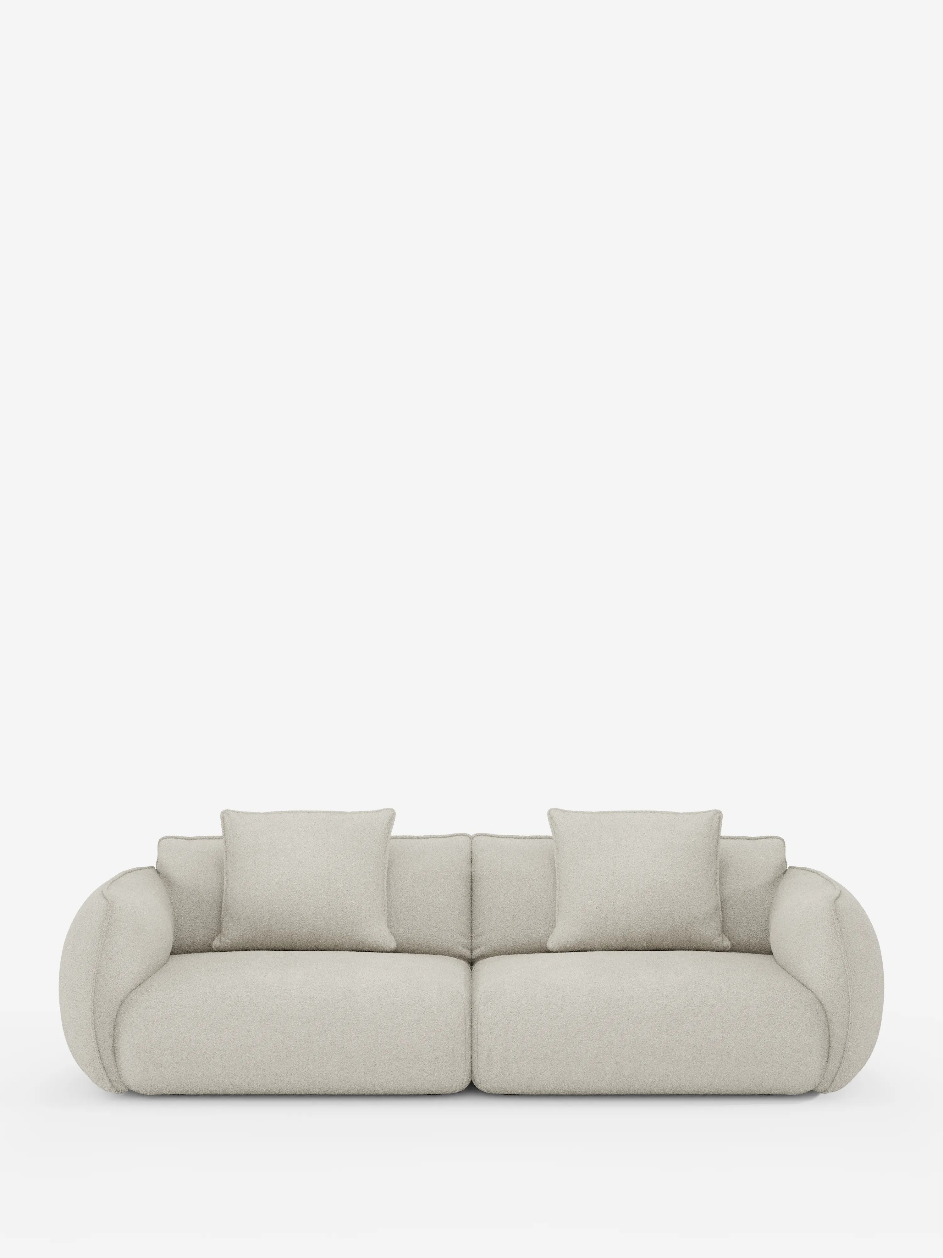Un moderno divano modulare a 3 posti Nimbus di divitt.sbs, rivestito in tessuto effetto cotone (t33) di colore beige chiaro e resistente alle macchie, dotato di due ampi cuscini di seduta e due cuscini dello schienale. I braccioli arrotondati e di grandi dimensioni conferiscono al divano un aspetto lussuoso e accogliente. Il divano è esposto su uno sfondo bianco a tinta unita.