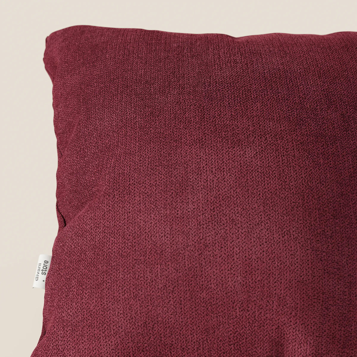 Primo piano del cuscino Destiny di divitt.sbs, disponibile in T02 rosso tessuto morbido impermeabile, su sfondo beige. Il cuscino presenta un sottile motivo, una fodera lavabile e una piccola etichetta bianca sul bordo sinistro.