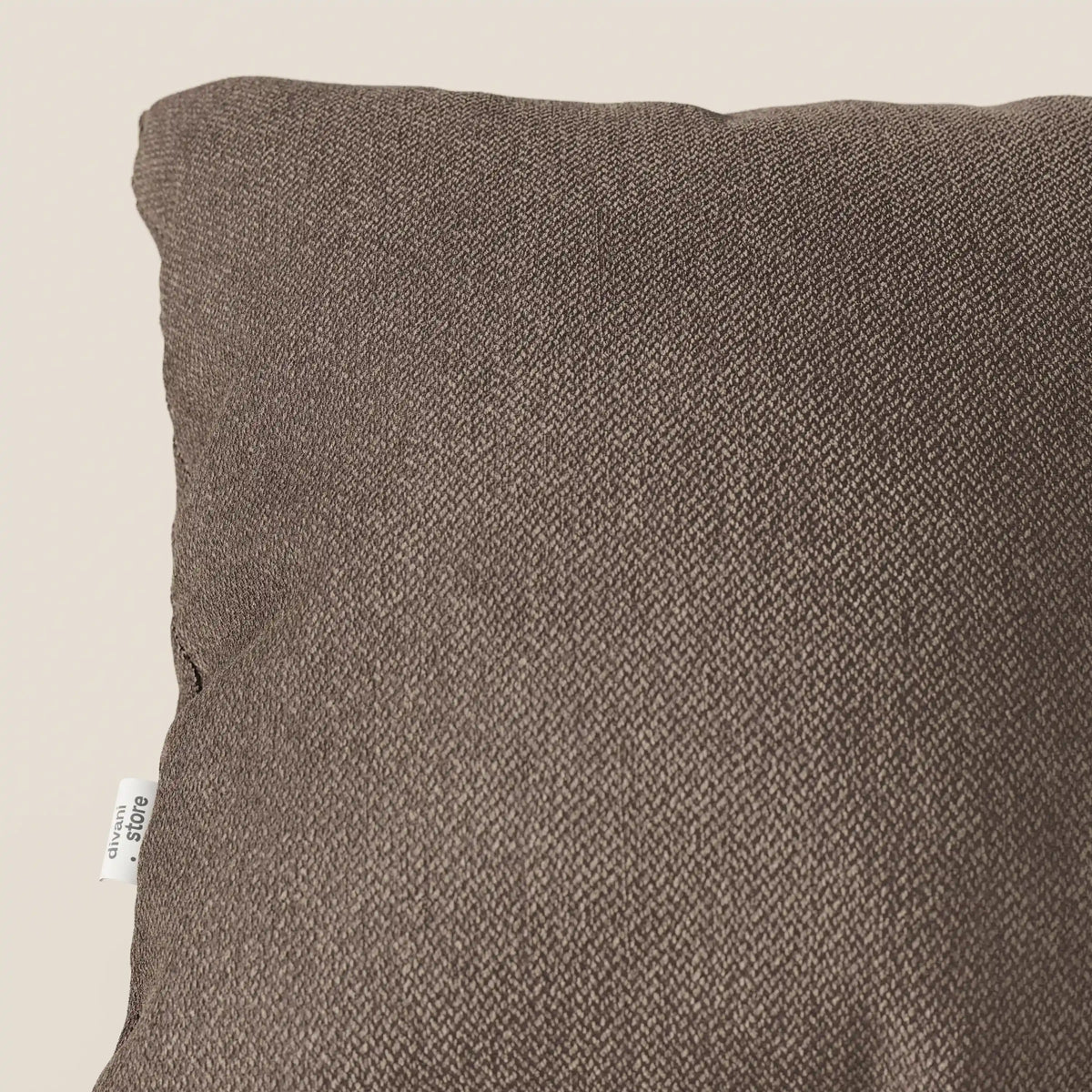 Primo piano di un cuscino Sogno di divitt.sbs in morbido tessuto SMACCHIABILE T05 marrone, caratterizzato da un sottile motivo intrecciato e da una piccola etichetta bianca. Solo la parte superiore sinistra è visibile su uno sfondo beige chiaro.