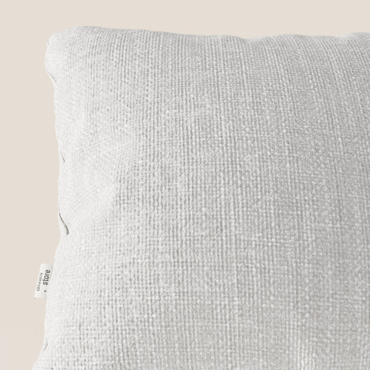 Primo piano del cuscino Lyon 45x45 cm in morbido tessuto intrecciato impermeabile T06 grigio chiaro di divitt.sbs, su sfondo beige con etichetta bianca visibile che riporta le informazioni sul materiale. Il cuscino appare morbido e ben rifinito.