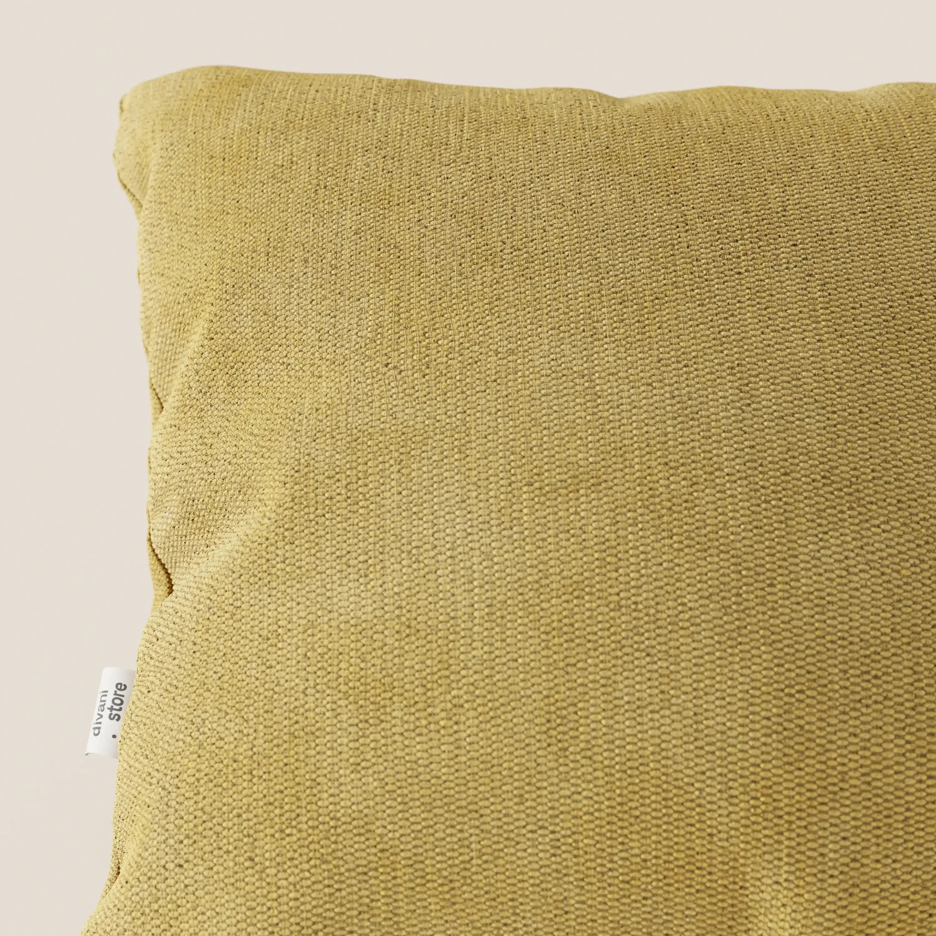 Primo piano del cuscino Miami 45x45 cm di divitt.sbs, in morbido tessuto impermeabile T14 giallo con etichetta "urban" bianca, su sfondo neutro. Di questo cuscino è visibile solo la parte superiore sinistra.