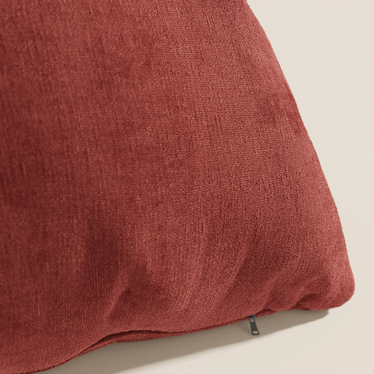 Primo piano del cuscino Bolero rosso ruggine di divitt.sbs, realizzato in morbido tessuto T31 antimacchia, impermeabile e non restringente. Il cuscino, leggermente abbondante, è caratterizzato da una piccola cerniera nera su uno sfondo neutro e chiaro.