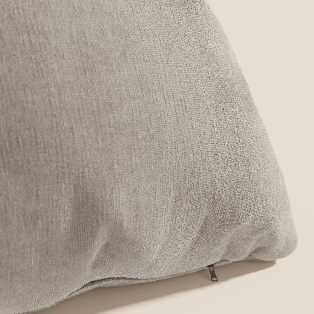 Primo piano del cuscino Bolero di divitt.sbs in grigio chiaro, con tessuto T31 morbido e testurizzato, resistente alle macchie, impermeabile e non restringente. Una piccola cerniera nera mostra il rivestimento sfoderabile su uno sfondo beige.