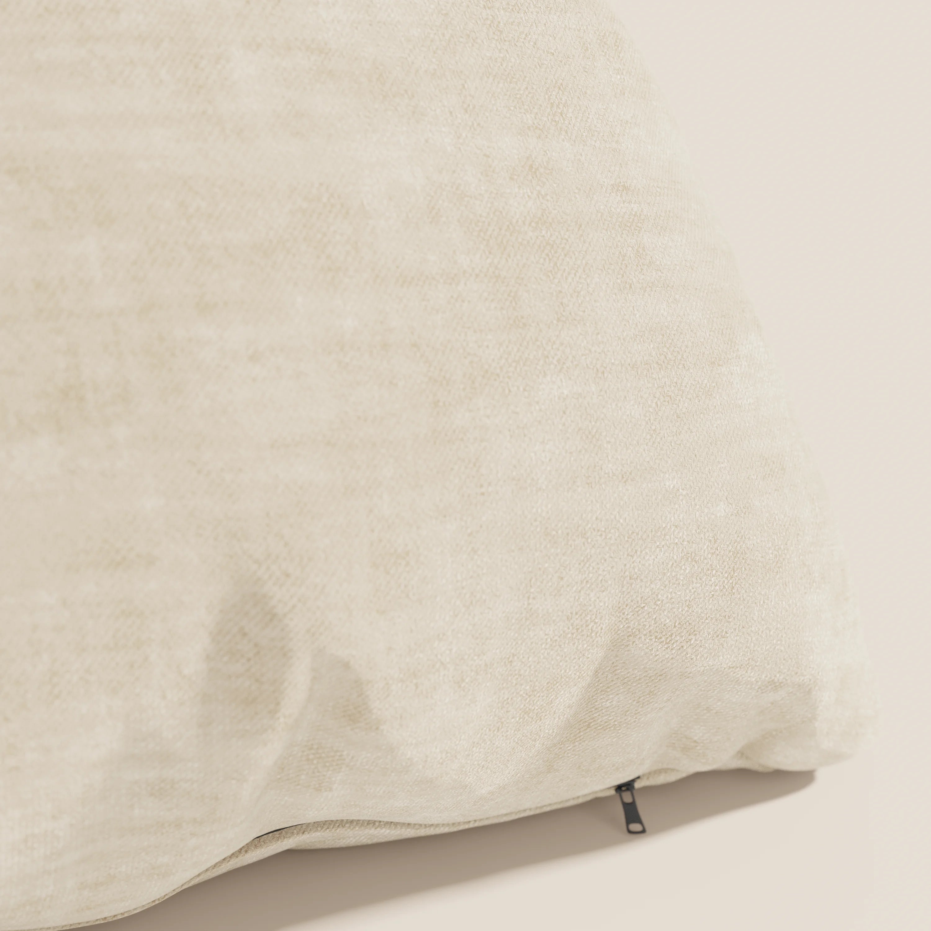 Primo piano del cuscino Sofia di divitt.sbs in beige chiaro, caratterizzato da pieghe morbide, una piccola cerniera nera e realizzato in velluto nuvolato Easy Clean T35 smacchiabile e impermeabile per un look neutro e rilassante.