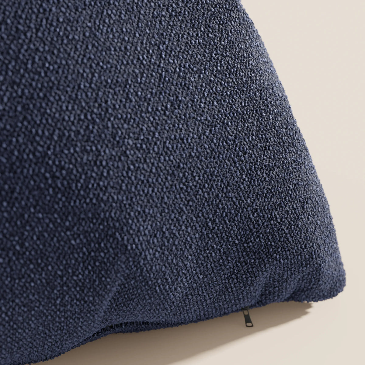 Primo piano del cuscino Lambada di divitt.sbs in blu navy, caratterizzato da un tessuto T33 testurizzato, smacchiabile e impermeabile, con un piccolo tiretto nero in corrispondenza della cucitura, su uno sfondo beige chiaro.