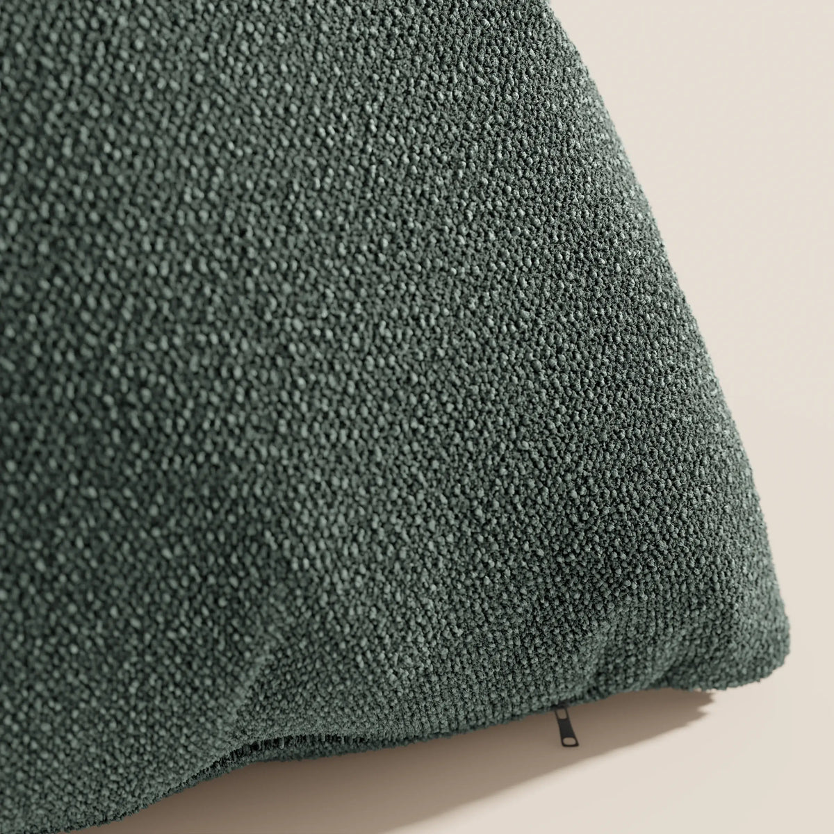 Primo piano del cuscino Lambada di divitt.sbs in verde scuro, realizzato con un tessuto di cotone fresco, antimacchia e impermeabile di aspetto naturale (T33), con una trama ad anelli. Il cuscino poggia su uno sfondo beige chiaro, con il tiretto della cerniera visibile in basso.