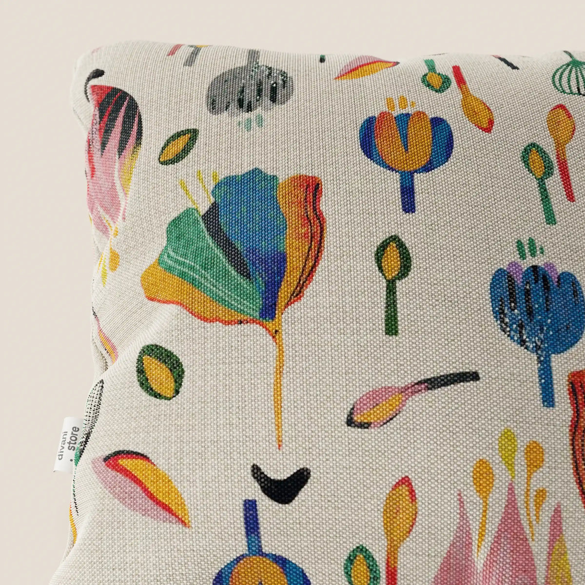 Un primo piano del cuscino divitt.sbs Joy collezione 45x45 cm mostra la sua fantasia floreale astratta multicolore su un fresco cotone panna impermeabile. Un cartellino in tessuto bianco si trova sul lato, su uno sfondo chiaro e neutro.