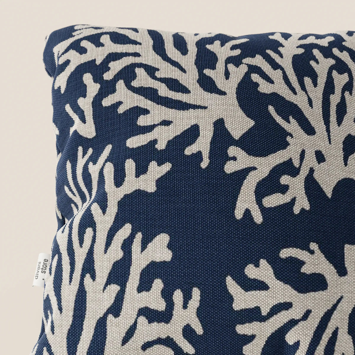 Primo piano di un cuscino divitt.sbs Nautilus 45x45 in tessuto impermeabile coralli, caratterizzato da uno sfondo blu navy con un motivo di barriera corallina bianca e un'etichetta bianca visibile sul bordo sinistro.