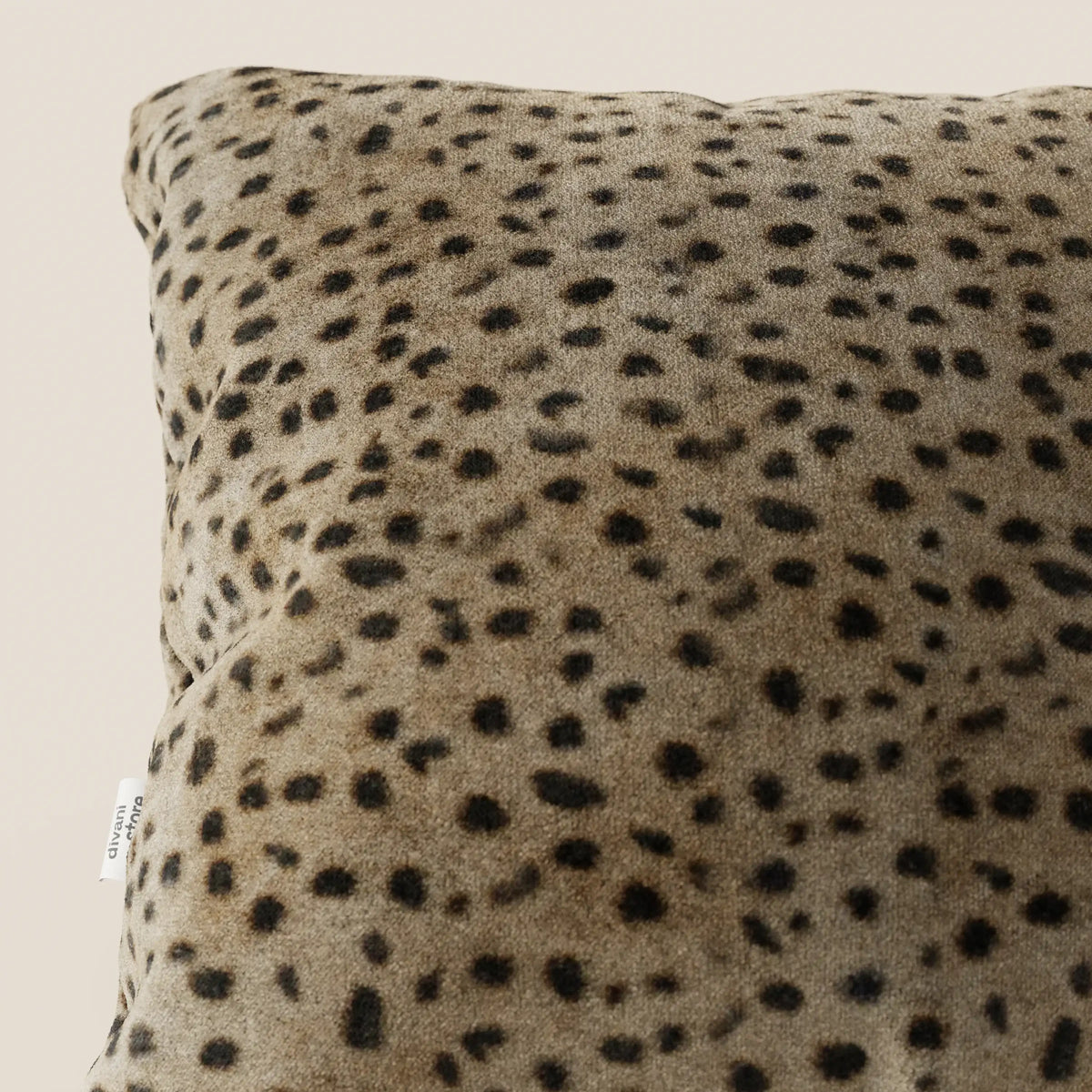 Primo piano del cuscino Wild 45x45 di divitt.sbs della collezione Wild, in microfibra impermeabile con stampa ghepardo. Una piccola etichetta bianca si trova sul bordo inferiore sinistro, con uno sfondo beige chiaro.