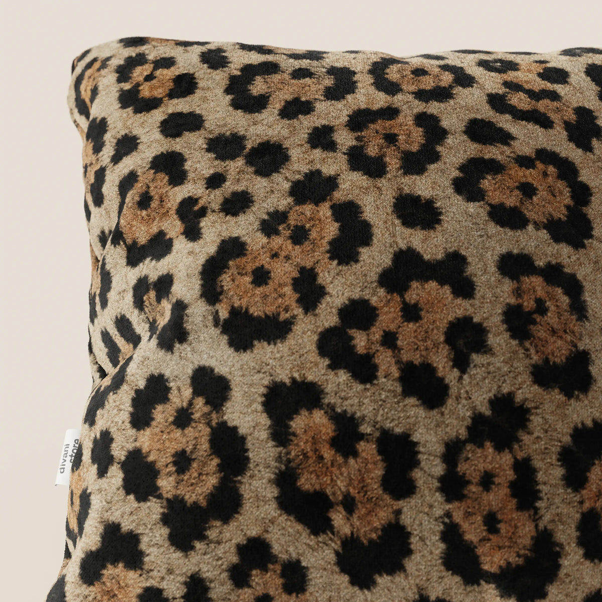 Primo piano del cuscino divitt.sbs Wild in collezione Wild in microfibra impermeabile giaguaro, caratterizzato da un morbido tessuto leopardato e da una piccola etichetta bianca sulla cucitura su uno sfondo beige chiaro.