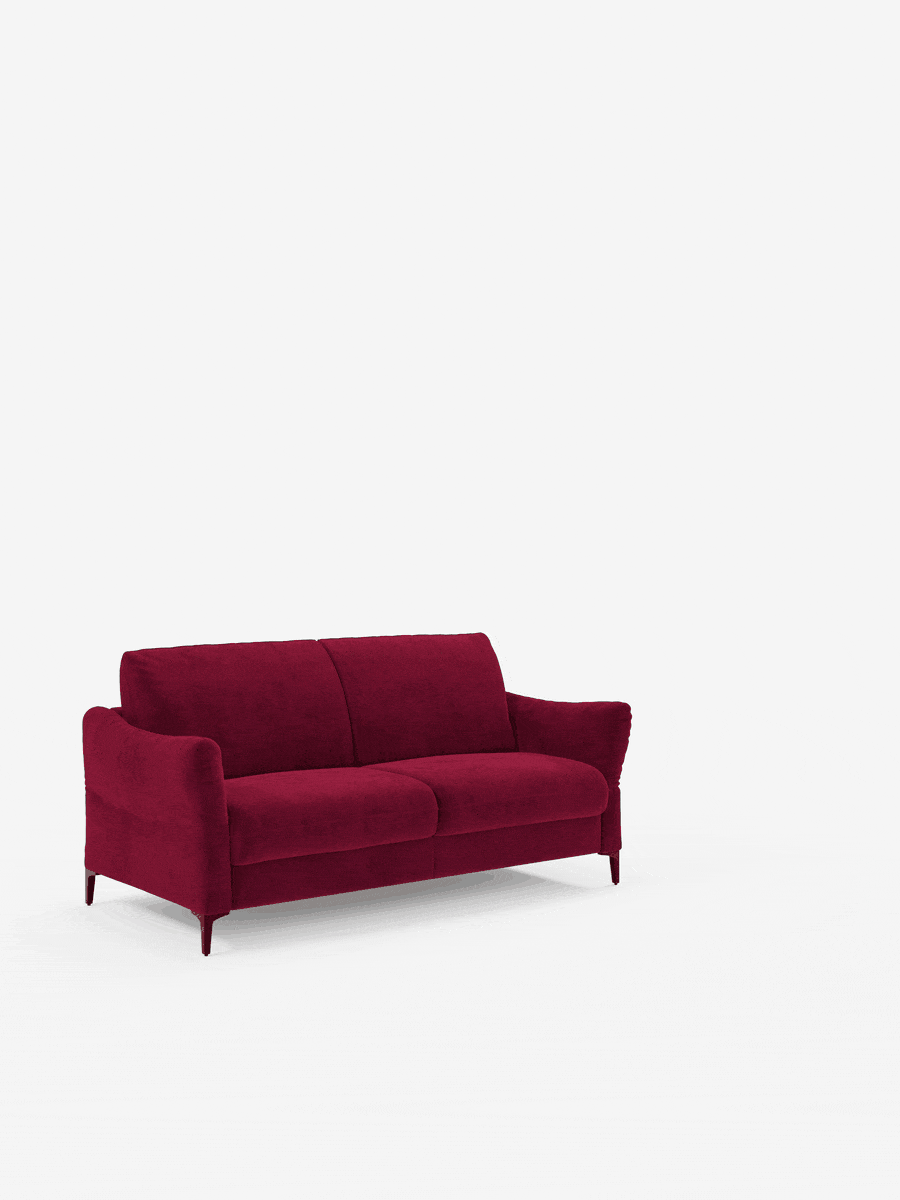 Un divano letto Dalia di divitt.sbs in stile contemporaneo, rivestito in tessuto T30 di velluto rosso intenso e resistente alle macchie, con braccioli ricurvi e gambe sottili, è posto al centro di uno sfondo bianco liscio. Il divano è dotato di due cuscini di seduta e due cuscini di schienale che gli conferiscono un aspetto morbido e accogliente. L’ambiente è minimalista e ordinato.