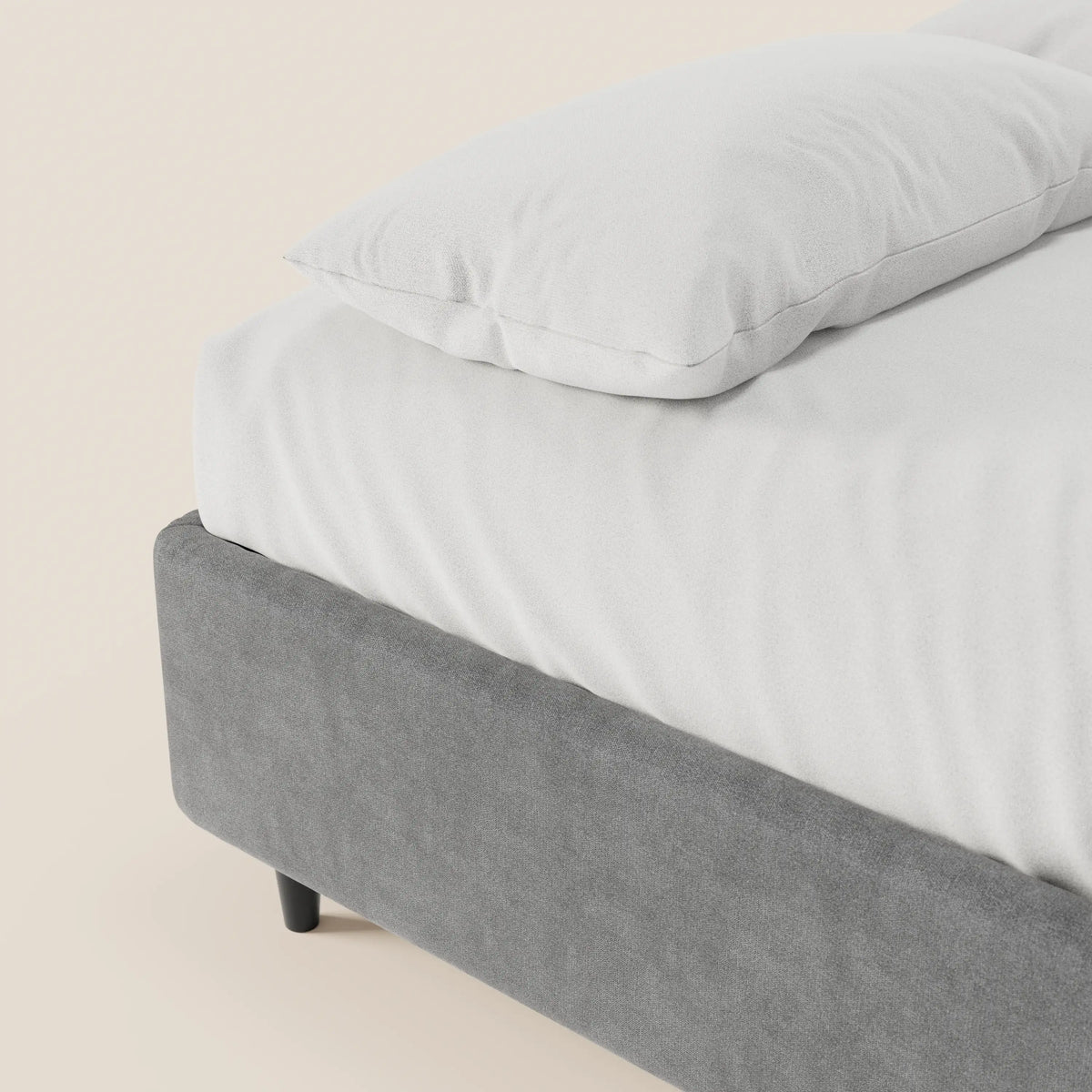 Il letto sommier imbottito ERON con vano contenitore in tessuto impermeabile certificato Oeko-Tex di Letti.store presenta una base imbottita grigia con gambe corte nere, un lenzuolo con angoli bianco e un cuscino coordinato su uno sfondo chiaro.