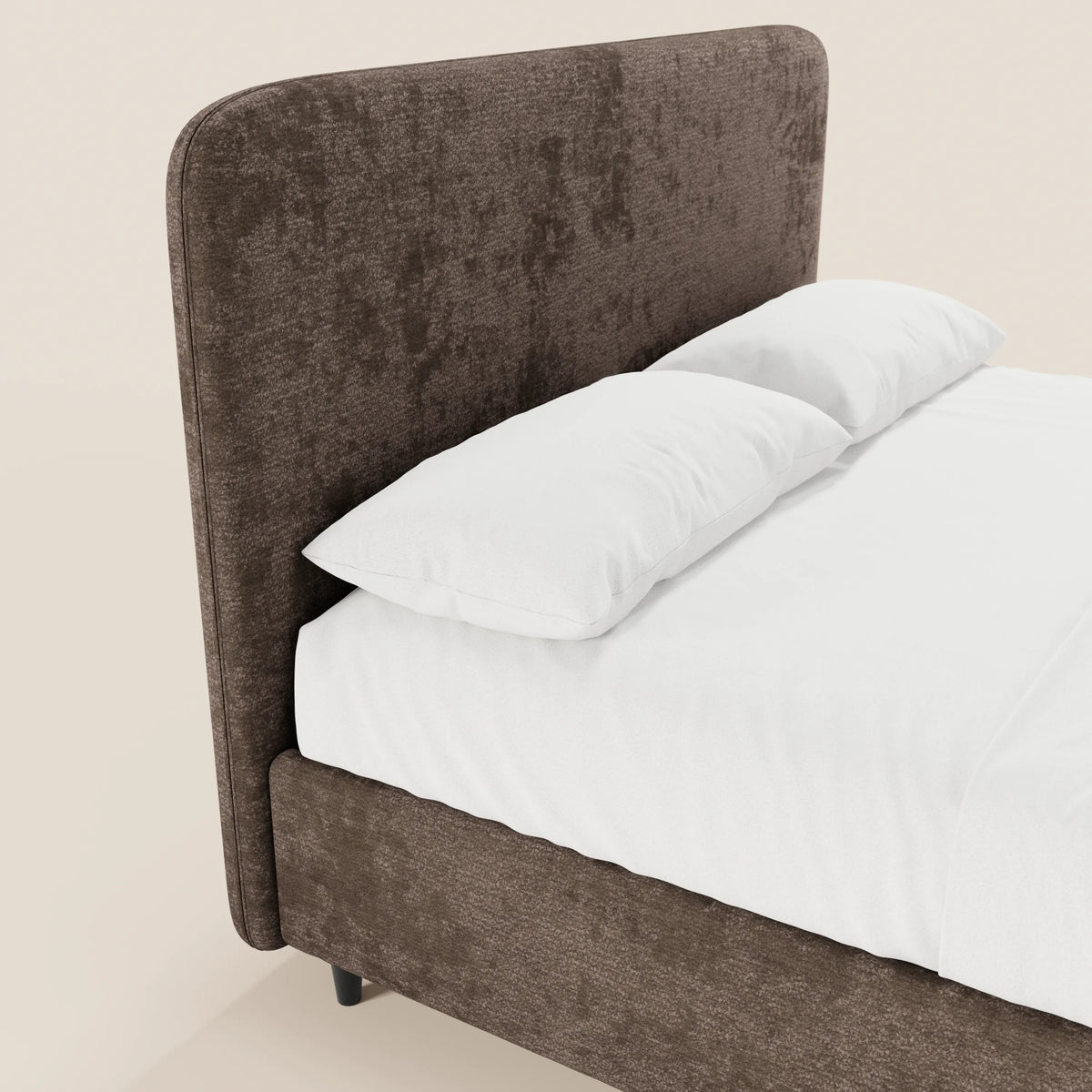 Un primo piano del letto imbottito KAELOS minimal di Letti.store mette in risalto la sua testiera alta e arrotondata in ciniglia marrone. Abbinato a lenzuola e cuscini di un bianco candido, solo una parte del letto, con le gambe alte e il vano contenitore, è visibile su uno sfondo semplice.