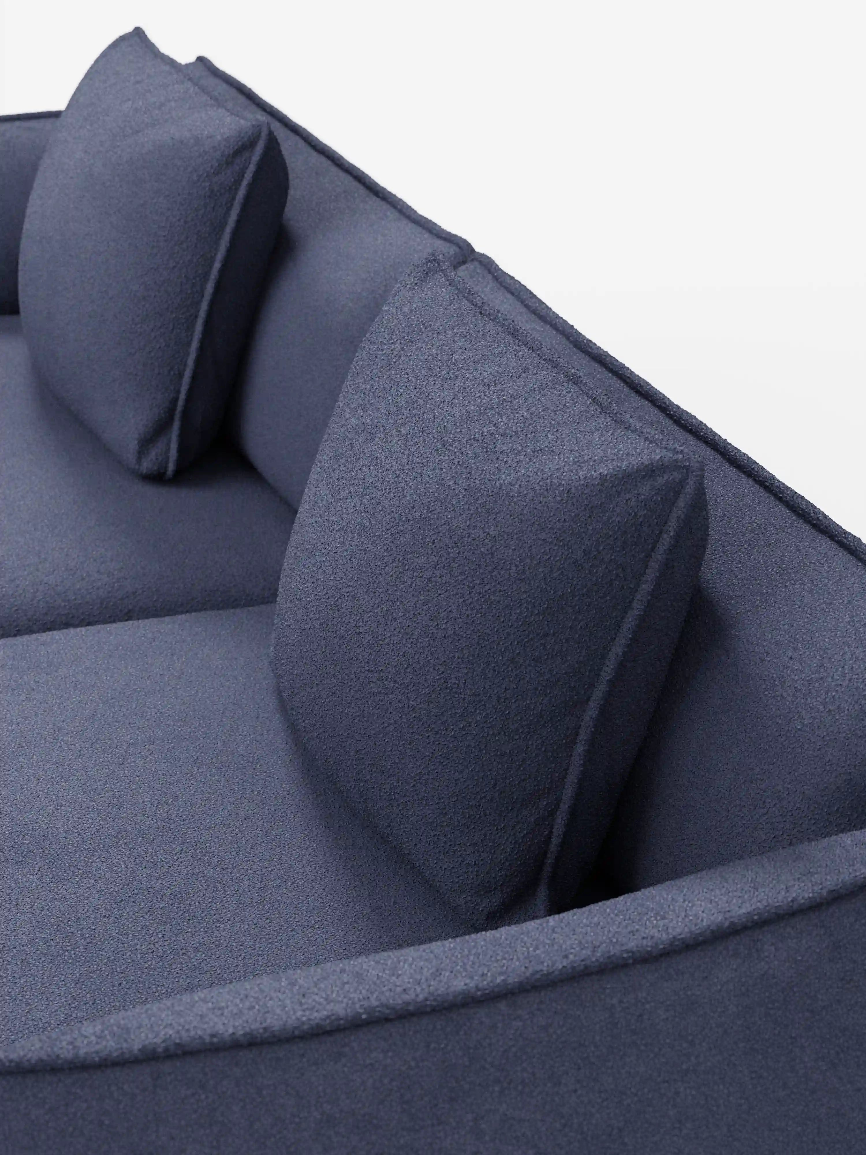Una vista ravvicinata dall'alto del divano modulare e componibile Nimbus di divitt.sbs, a 3 posti, da 250 cm, in blu scuro, rivestito in tessuto lavabile e antimacchia effetto cotone t33. Questo divano moderno presenta un design minimalista dalle linee pulite, un rivestimento liscio, braccioli leggermente arrotondati ed è dotato di due cuscini quadrati coordinati per lo schienale, il tutto su uno sfondo bianco a tinta unita.