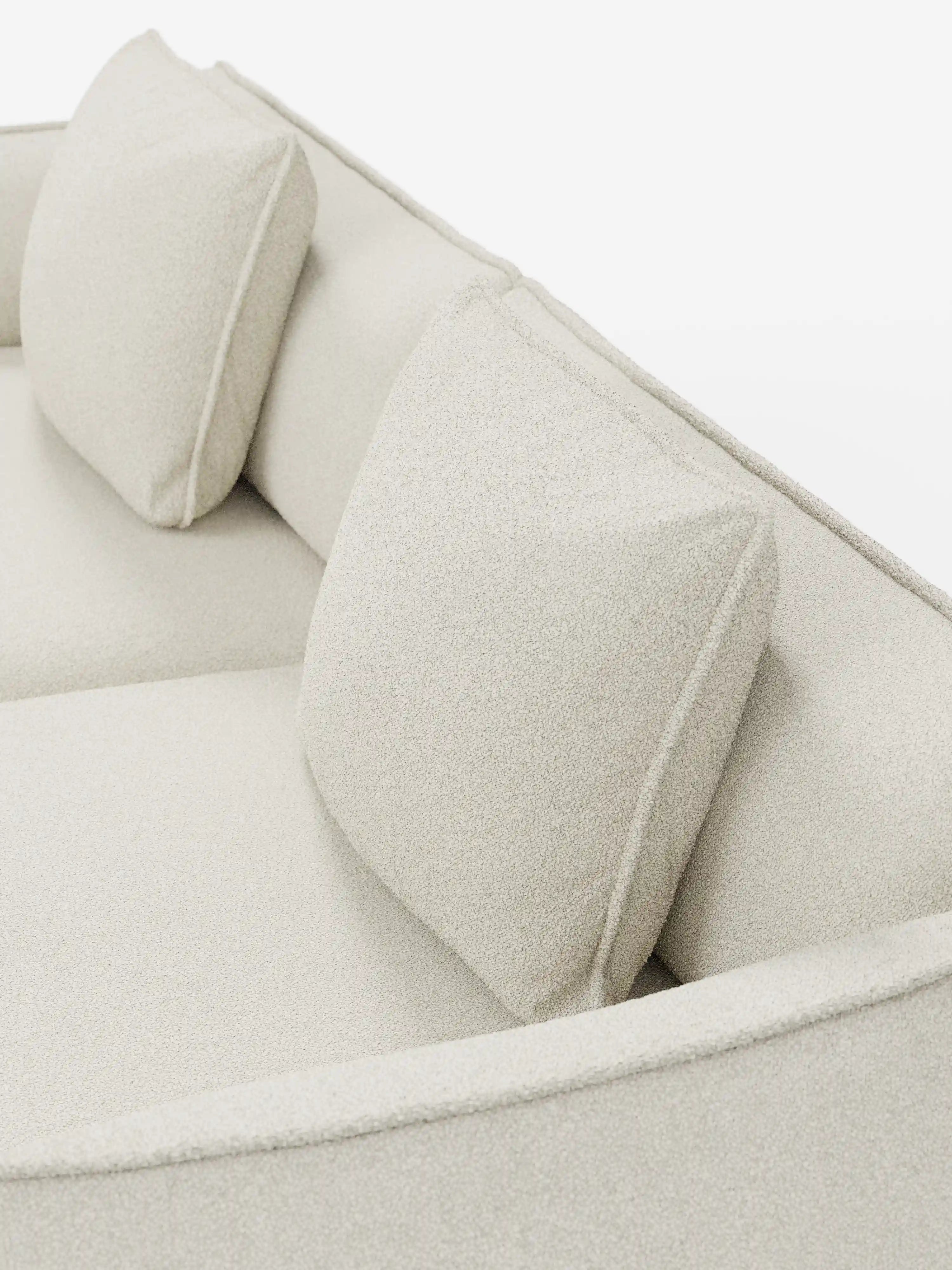 Primo piano del divano modulare e componibile Nimbus a 3 posti di divitt.sbs, rivestito in tessuto beige effetto cotone antimacchia (tessuto smacchiabile effetto cotone t33). Due cuscini quadrati coordinati poggiano contro lo schienale basso del divano. La morbida trama è chiaramente visibile sotto una luce intensa, accentuando le linee moderne e minimaliste e la versatile modularità di questo divano contemporaneo da 250 cm.