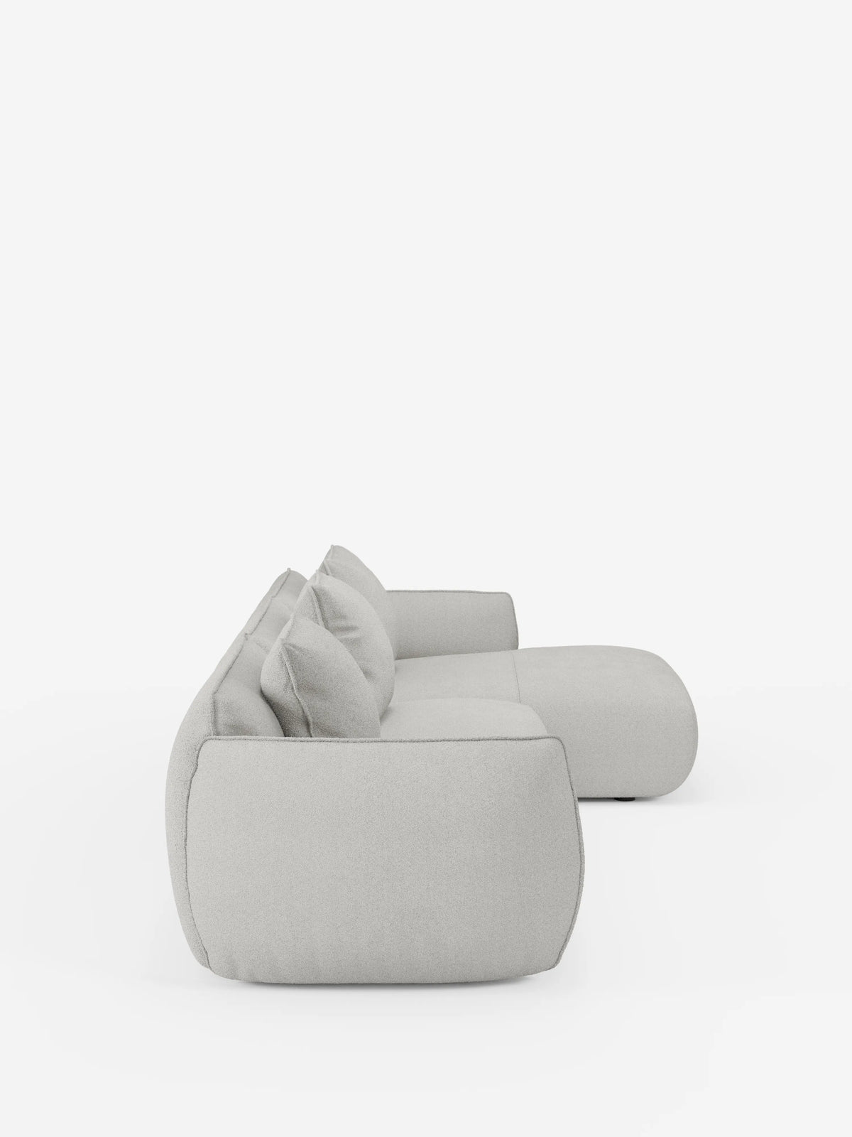 Vista laterale del divano angolare con penisola componibile Nimbus in morbido tessuto effetto cotone smacchiabile T33 di divitt.sbs, caratterizzato da un design modulare moderno in grigio chiaro con due grandi cuscini dello schienale e bordi arrotondati, su uno sfondo bianco a tinta unita. Questo divano presenta uno stile minimalista e contemporaneo con un rivestimento morbido e soffice.