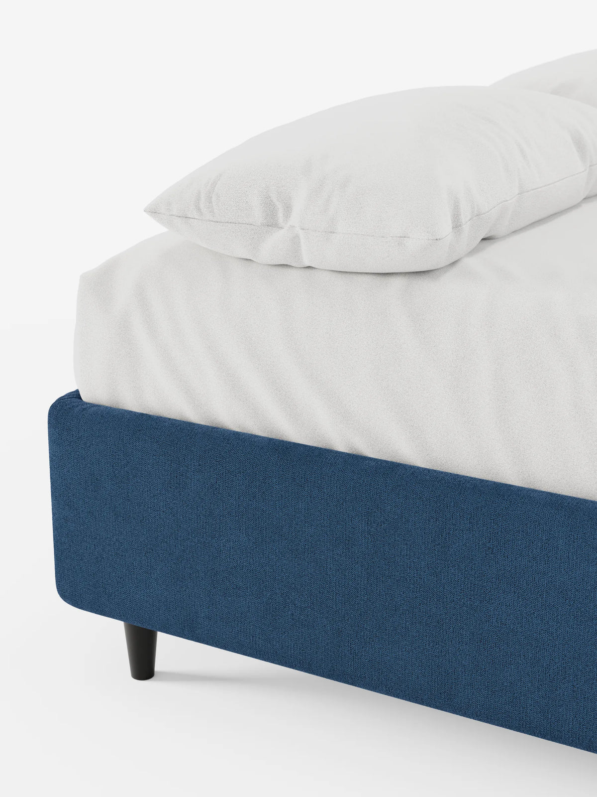 Un primo piano di un letto sommier imbottito ERON con contenitore, rivestito in tessuto impermeabile certificato Oeko-Tex in tessuto testurizzato blu navy, con lenzuolo bianco e cuscino, su piedini corti scuri, su uno sfondo bianco.