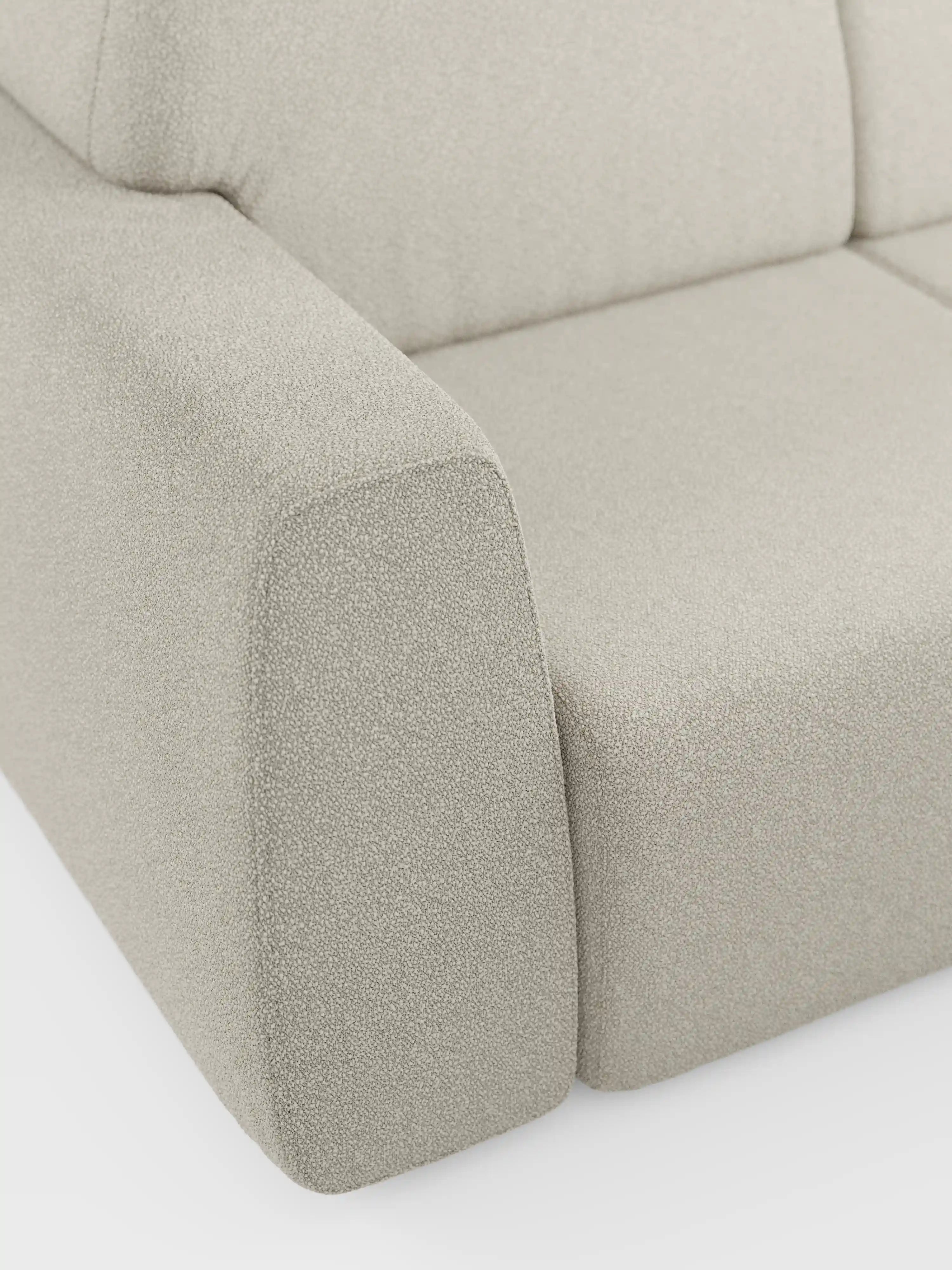 Primo piano del bracciolo e del cuscino di seduta del divano Orbit a 2 e 3 posti con sedute scorrevoli di divitt.sbs, rivestito in tessuto smacchiabile effetto cotone T33 color beige chiaro. Il tessuto presenta una trama delicata e leggermente ruvida. Questo divano moderno, completamente sfoderabile, si caratterizza per le linee pulite e il design moderno e minimalista. Lo sfondo è a tinta unita e bianco.
