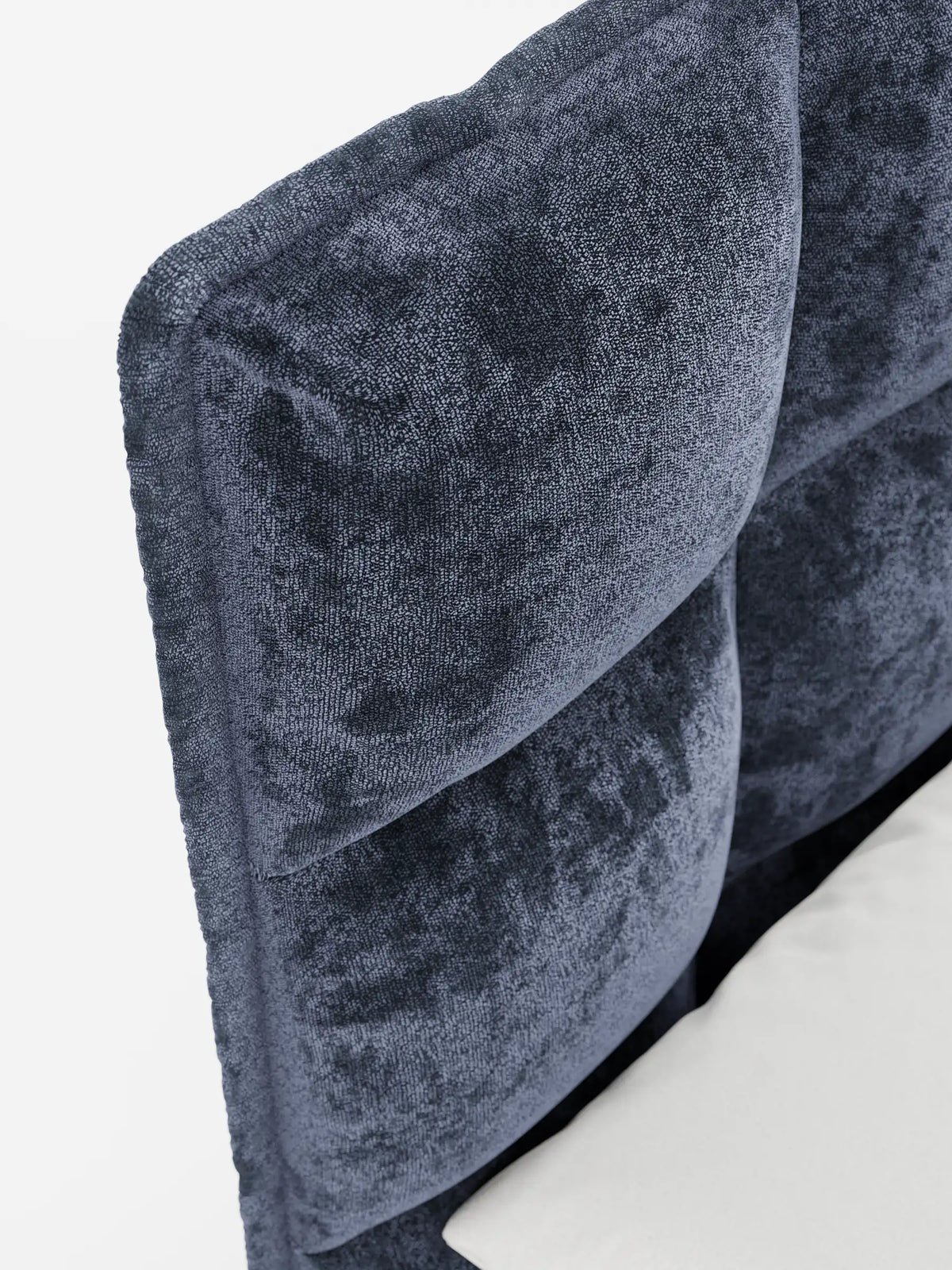 Primo piano della testiera capitonné blu scuro a ciuffetti di un letto imbottito AURO con vano contenitore e testiera capitonné alta in ciniglia Oeko-Tex®, caratterizzata da morbide sezioni a griglia e da un tessuto soffice accanto a un cuscino bianco.
