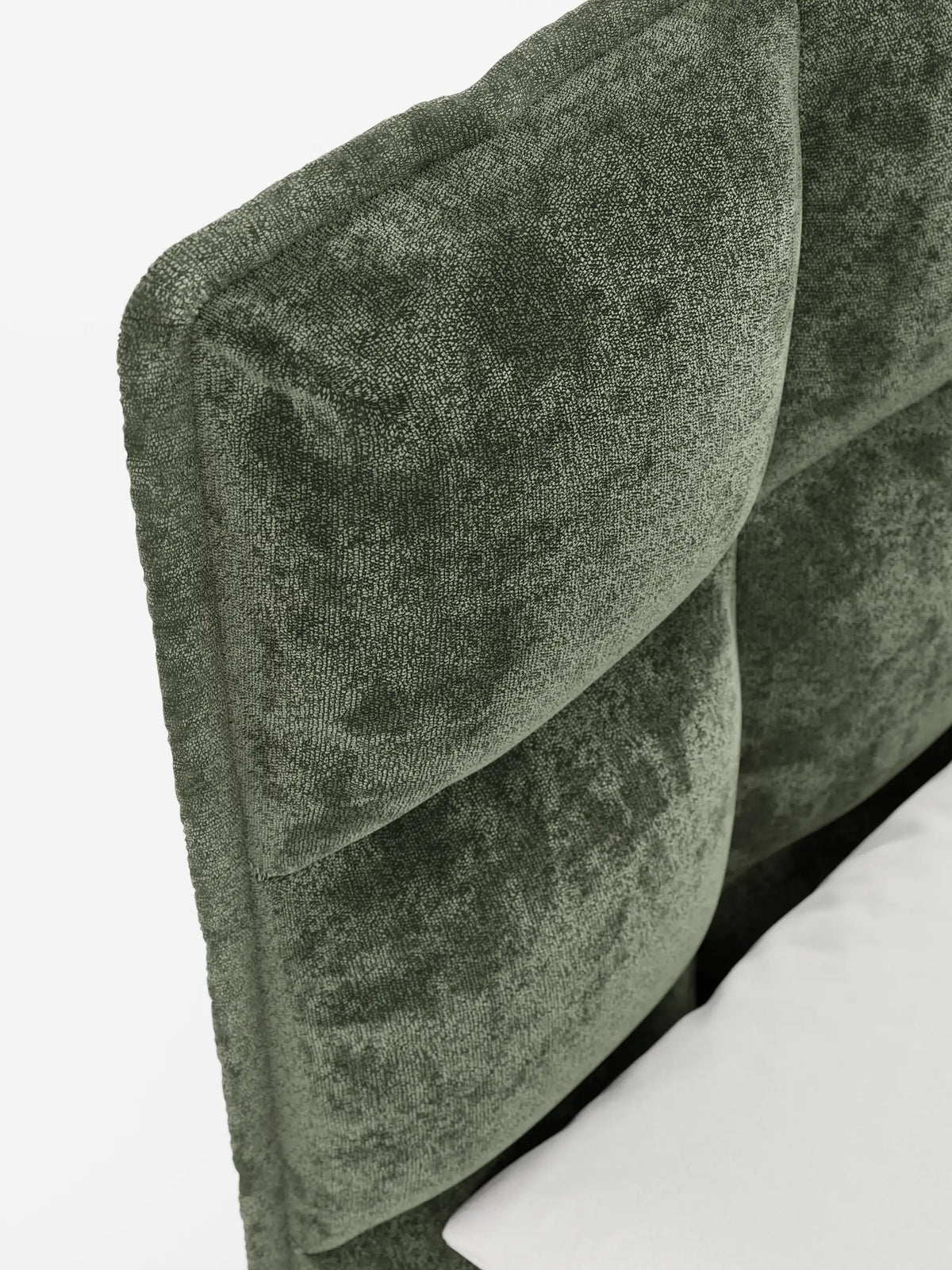 Primo piano del letto imbottito AURO con contenitore e testiera capitonné alta in ciniglia Oeko-Tex®: una testiera verde oliva con finitura capitonné, dalla consistenza morbida simile al velluto, con pannelli rettangolari su uno sfondo bianco a tinta unita.
