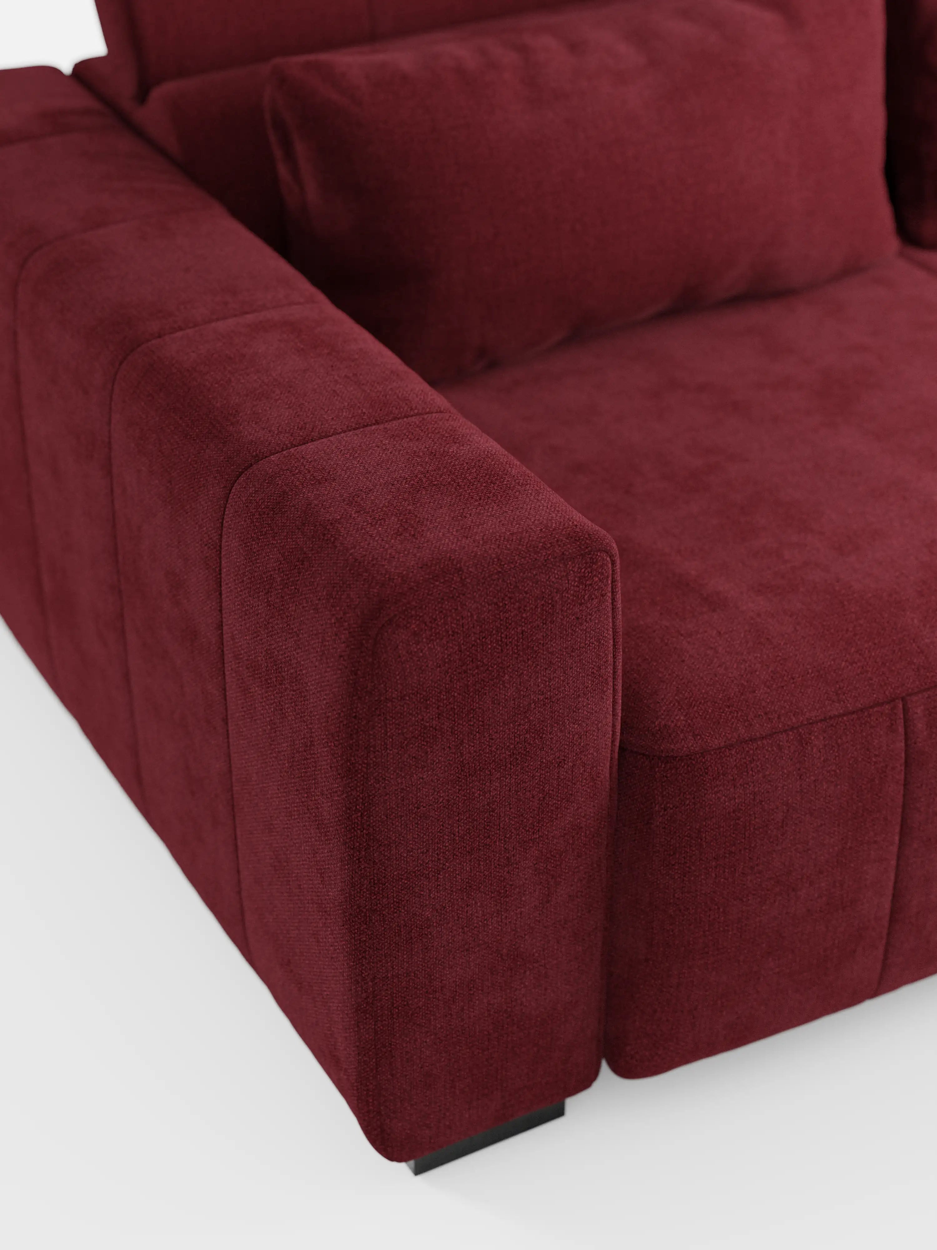 Primo piano del divano a 3 posti Doric di divitt.sbs, che ne mette in risalto il design moderno rivestito in tessuto T23 rosso intenso e resistente alle macchie. L'immagine evidenzia il bracciolo, la seduta e una parte del cuscino dello schienale, rivelando un rivestimento soffice e morbido con cuciture a vista e bordi squadrati ben definiti. Le sedute allungabili tramite relax elettrico e i poggiatesta reclinabili sono parzialmente visibili su uno sfondo bianco.
