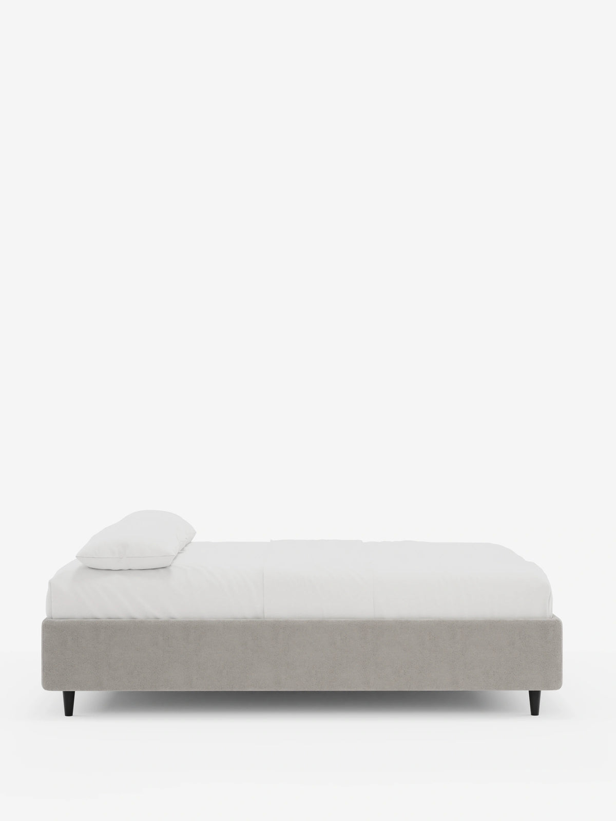 Letto ERON con rete imbottita e contenitore, rivestito in tessuto impermeabile certificato Oeko-Tex color grigio chiaro, caratterizzato da sottili gambe affusolate scure, un unico cuscino bianco e biancheria da letto bianca, in primo piano su uno sfondo bianco.