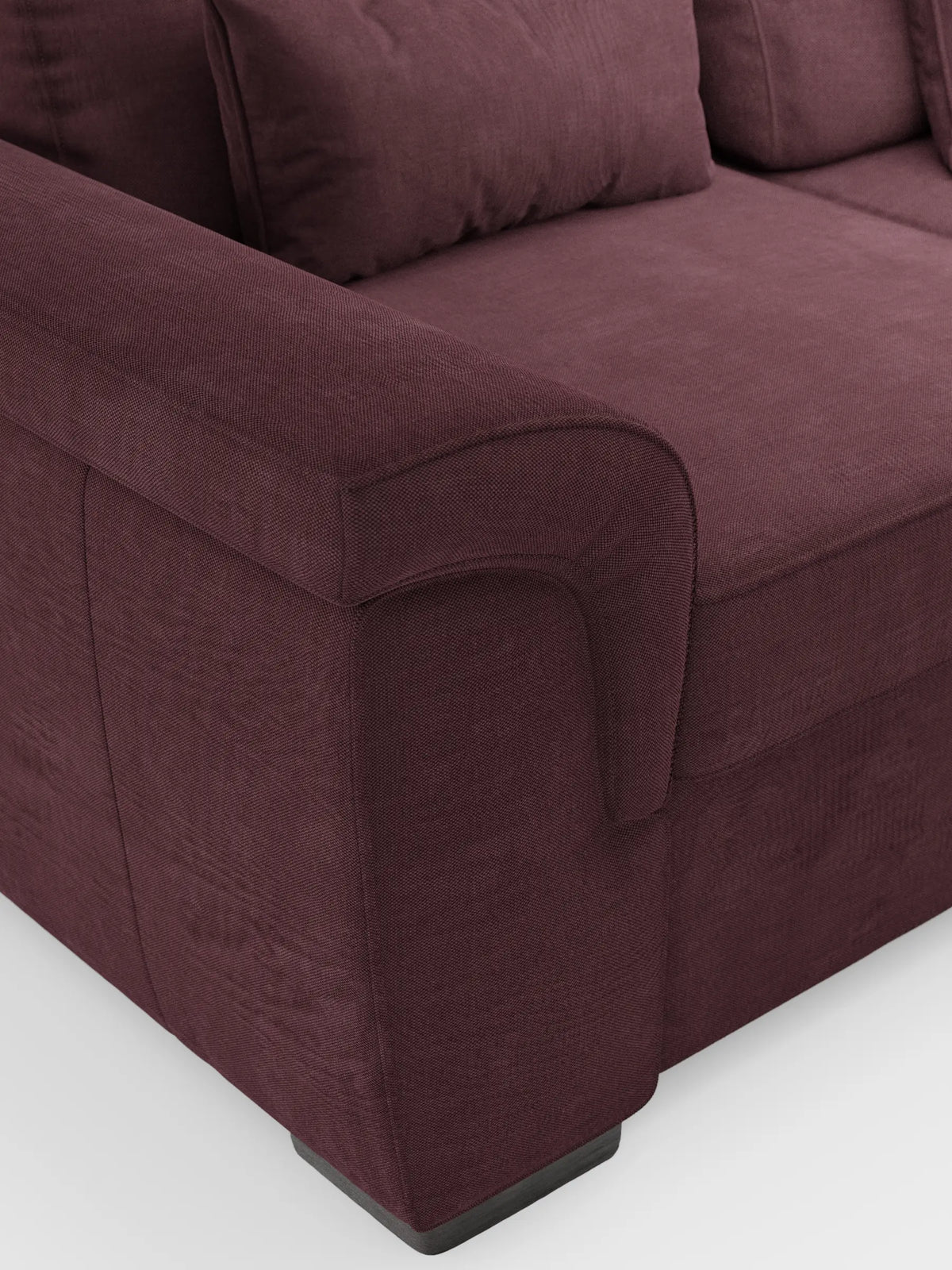 Un primo piano di un divano Ischia a 3 posti color prugna scuro con pouf estraibile e schienali scorrevoli, rivestito in tessuto misto lino lavabile, con particolare attenzione al bracciolo ricurvo, al rivestimento testurizzato e al morbido cuscino dello schienale, su uno sfondo bianco a tinta unita.