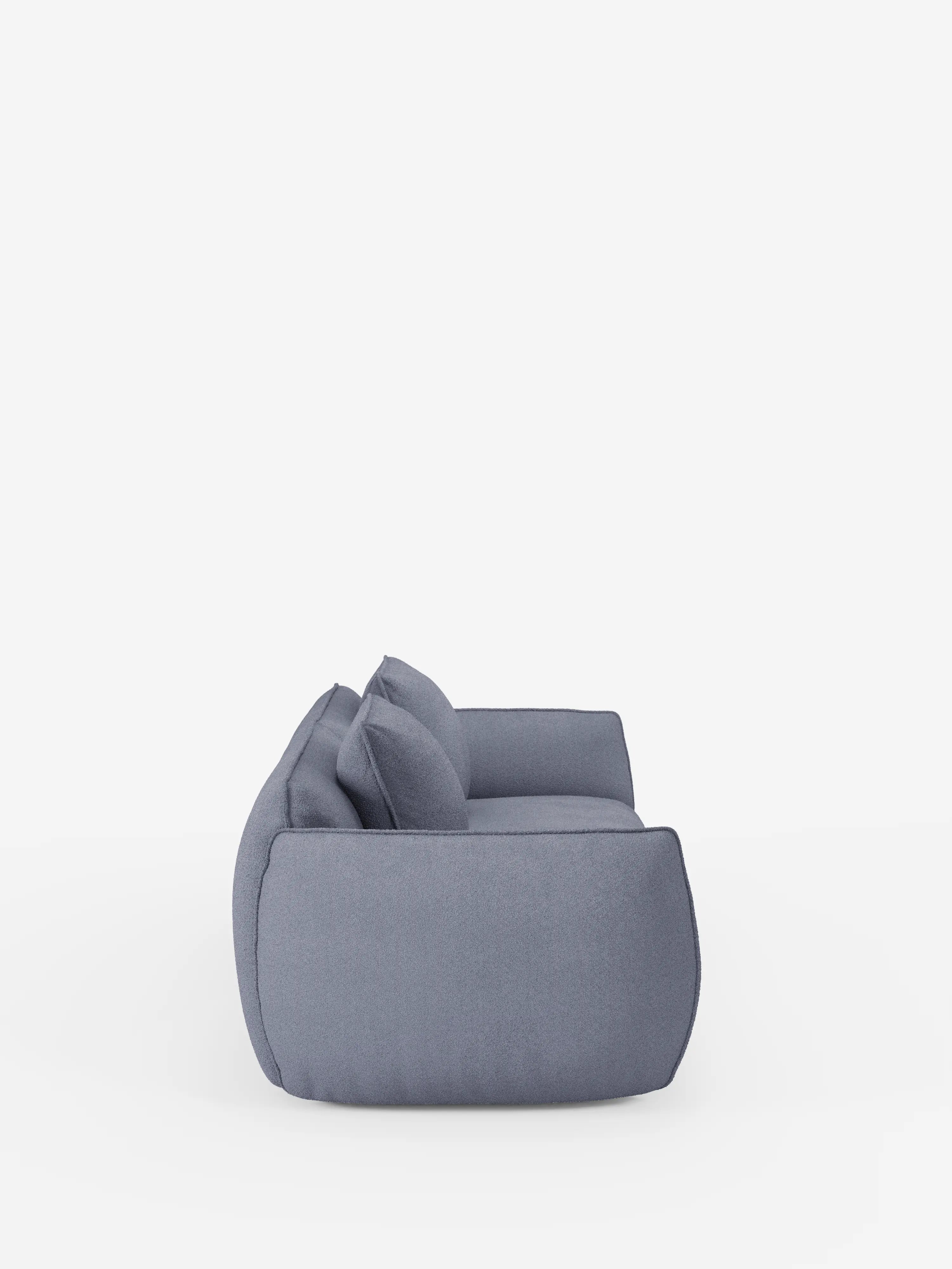 Una vista laterale del divano Nimbus a 3 posti, modulare e componibile, da 250 cm di divitt.sbs, rivestito in tessuto grigio effetto cotone antimacchia (t33), caratterizzato da morbidi cuscini e ampi braccioli. Su uno sfondo bianco a tinta unita, il divano presenta un design morbido e squadrato, con due cuscini dello schienale e un bracciolo ben visibili.