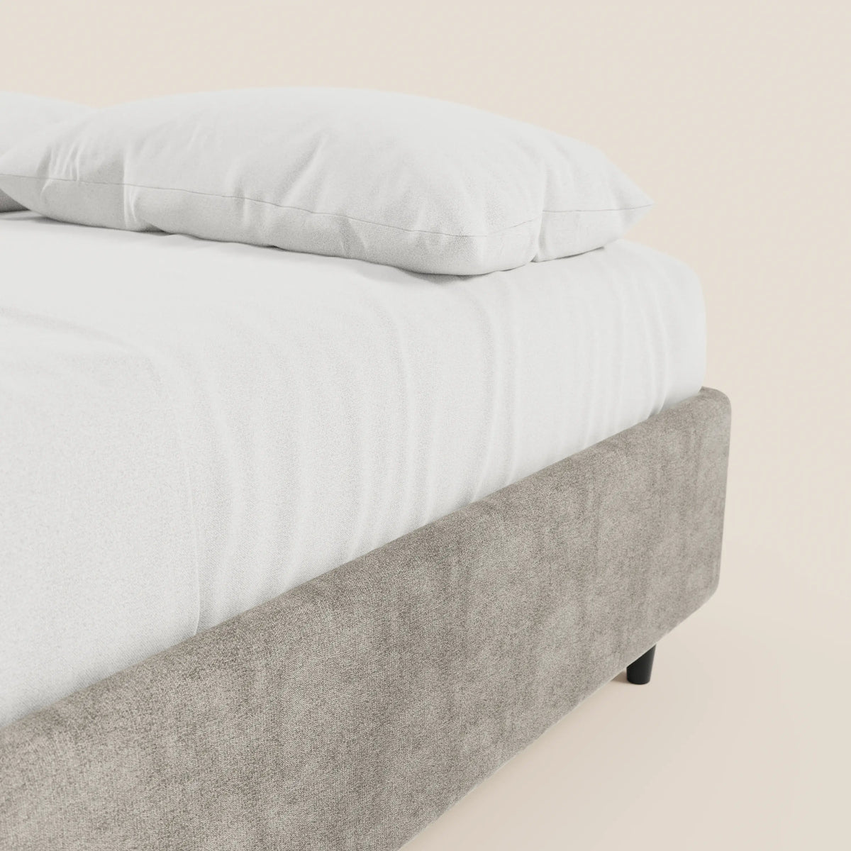 Un primo piano del letto sommier imbottito con contenitore ERON di Letti.store, realizzato con tessuto impermeabile certificato Oeko-Tex in grigio chiaro e dotato di gambe corte nere. Il letto, dalle finiture curate, fa da contrasto con una parete beige a tinta unita, creando un effetto pulito.
