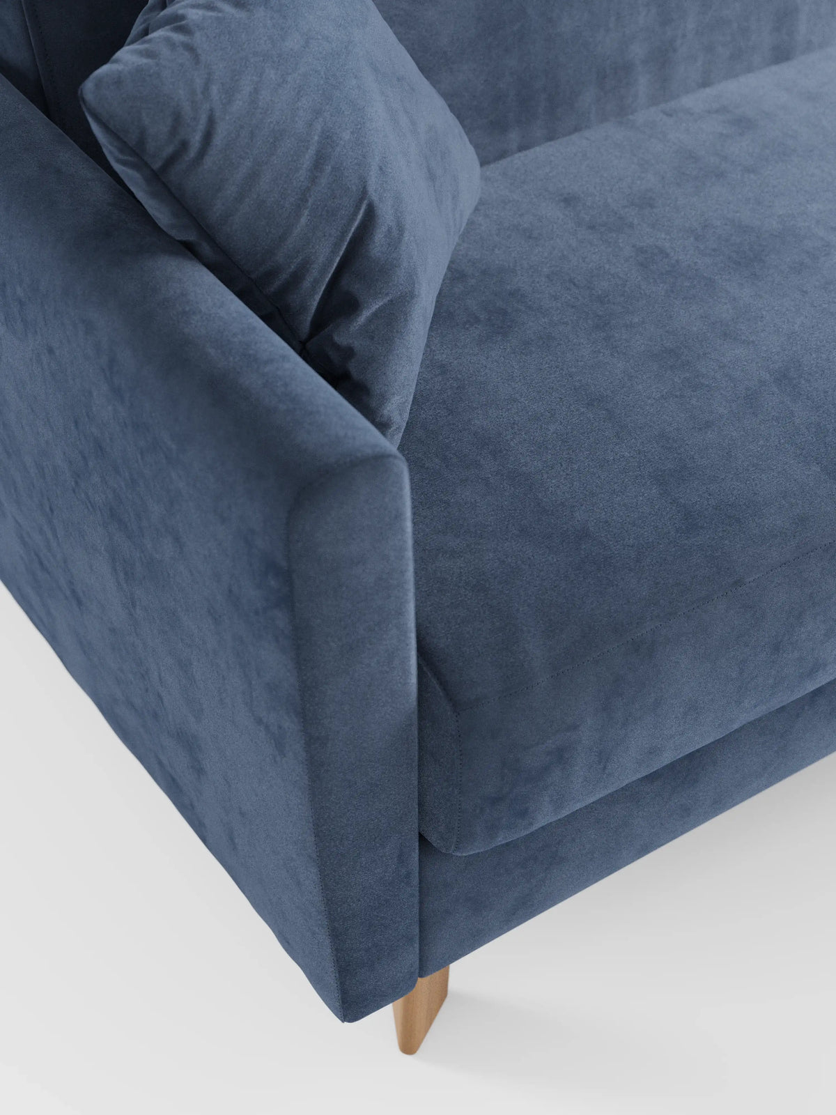 Primo piano di un divano letto Francy con poggiatesta regolabili di divitt.sbs, rivestito in morbido tessuto blu T30 resistente alle macchie. L’immagine mette in risalto il bracciolo, un cuscino coordinato e parte della seduta, evidenziando le linee pulite del divano e le gambe in legno chiaro su uno sfondo bianco a tinta unita. Il rivestimento è interamente sfoderabile per facilitare la pulizia.