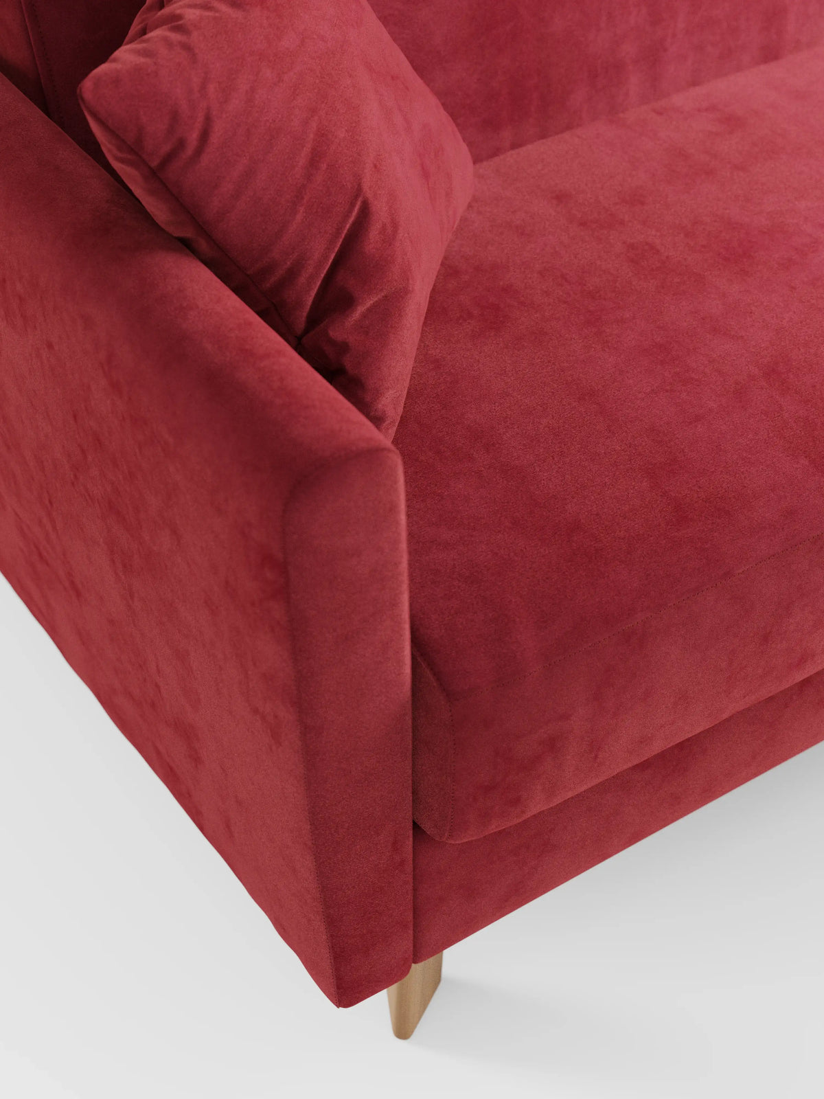 Un primo piano del divano letto Francy con poggiatesta regolabili di divitt.sbs in un rosso accattivante, con un cuscino abbinato che mette in risalto i braccioli angolati, la seduta e le gambe in legno. Il rivestimento è realizzato in elegante tessuto T30 resistente alle macchie, dall’aspetto morbido e dalla texture simile alla pelle scamosciata. Lo sfondo è una superficie bianca a tinta unita.