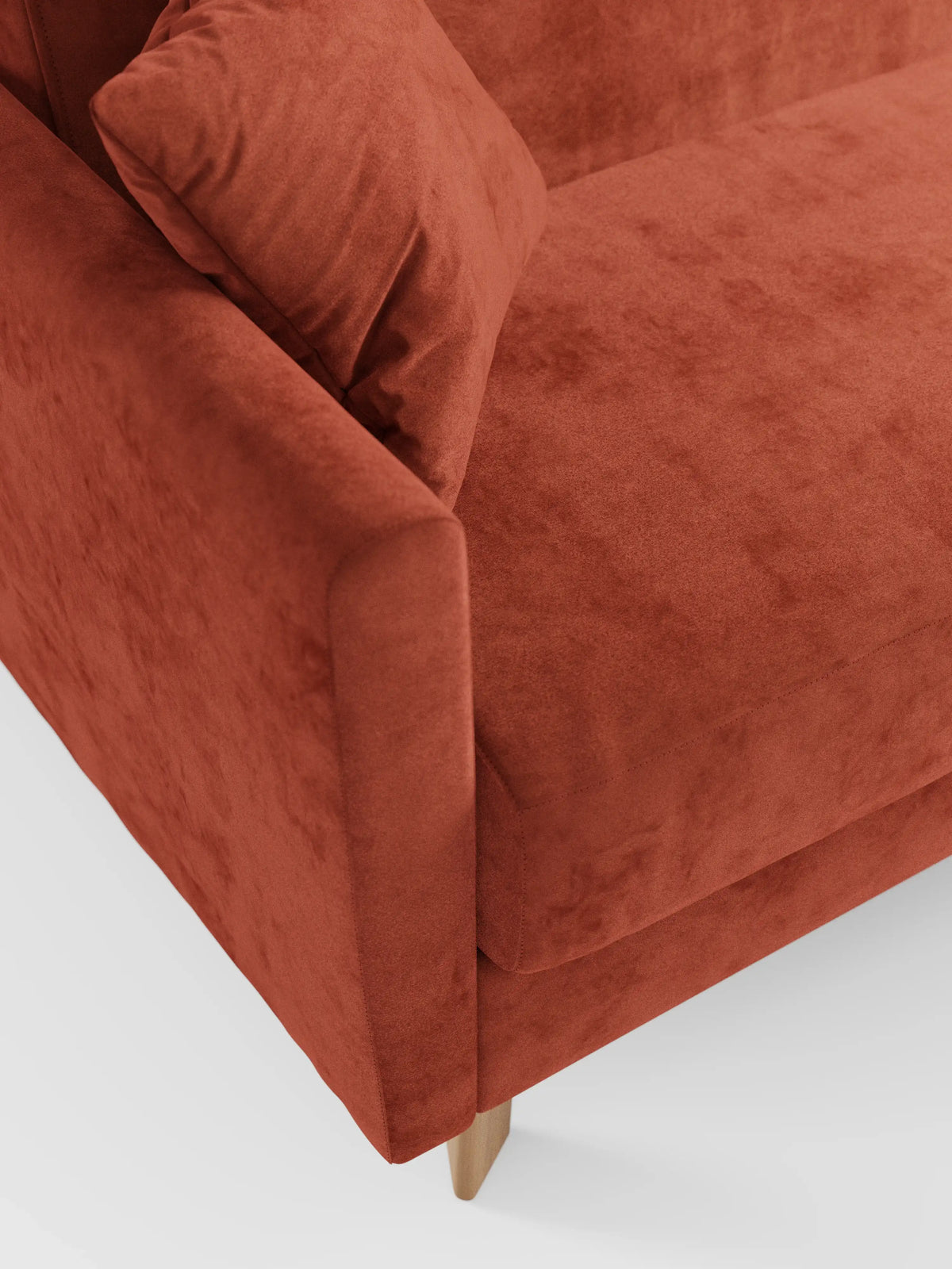 Primo piano di un divano letto Francy color ruggine con poggiatesta regolabili di divitt.sbs, caratterizzato da un rivestimento sfoderabile al 100% in elegante tessuto T30 antimacchia e da un cuscino coordinato sulla seduta. Questo moderno divano a 2 o 3 posti vanta linee pulite e gambe in legno chiaro, che risaltano su uno sfondo bianco a tinta unita.